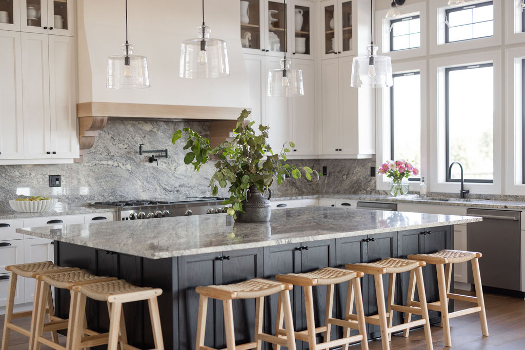 Modern kitchen with white cabinets, large windows, a central island with a plant, and bar stools.