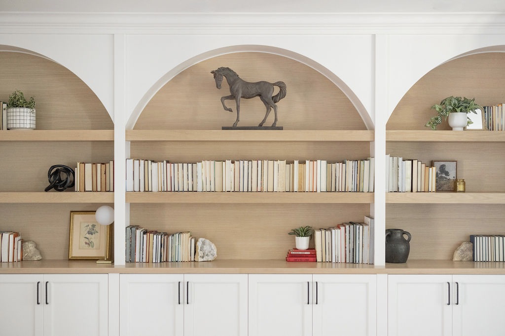 Bookshelf with a horse figurine on top, books, and decorative items, in a room with white walls and wooden shelves.