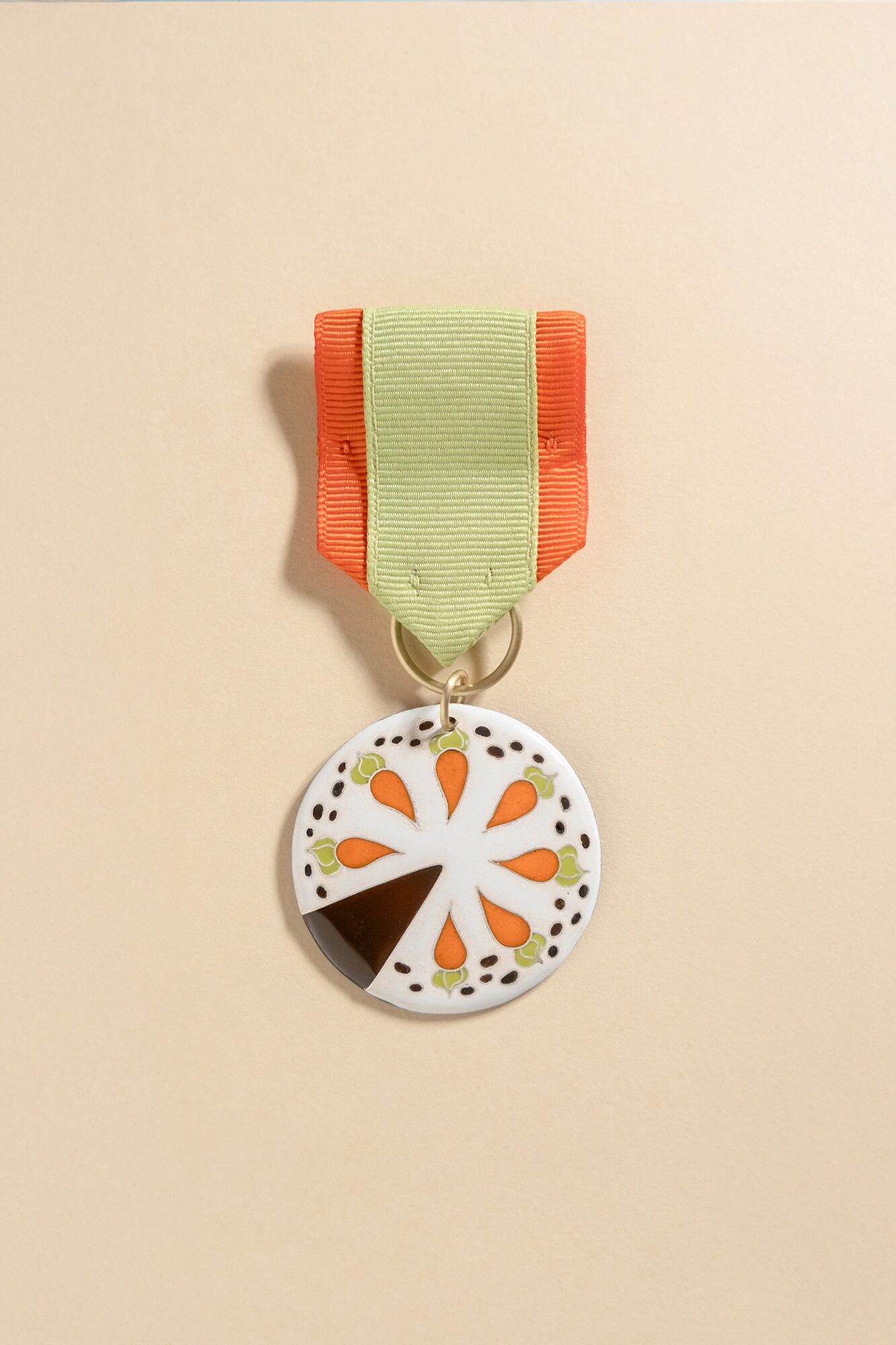 Colorful circular medal with orange, black, and white design, attached to a green and orange ribbon, on a plain background.