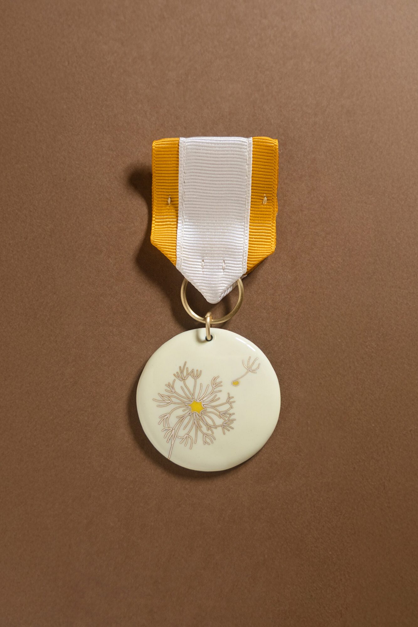 Medal with a white ribbon and yellow edges, circular medal with a snowflake design, on a brown background.