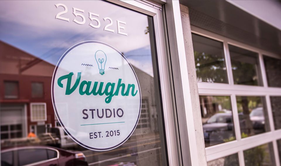 Glass window with Vaughan Studio logo, reflection of buildings and sky, and street view outside.