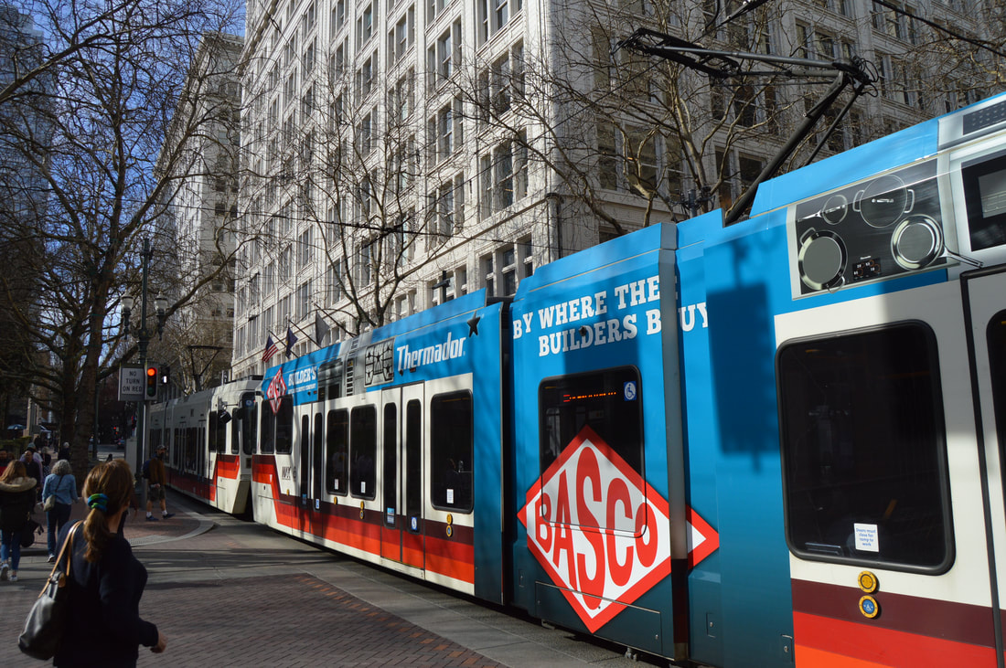 Streetcar with blue and white exterior, city buildings, and pedestrians on sidewalk.