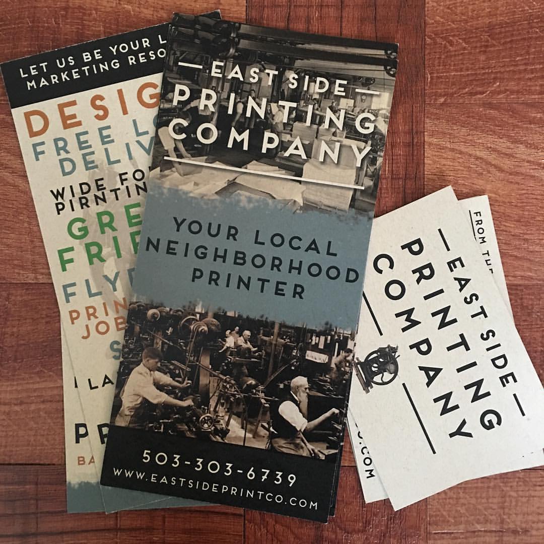 Business cards and flyers for East Side Printing Company on a wooden surface, featuring contact info and services.