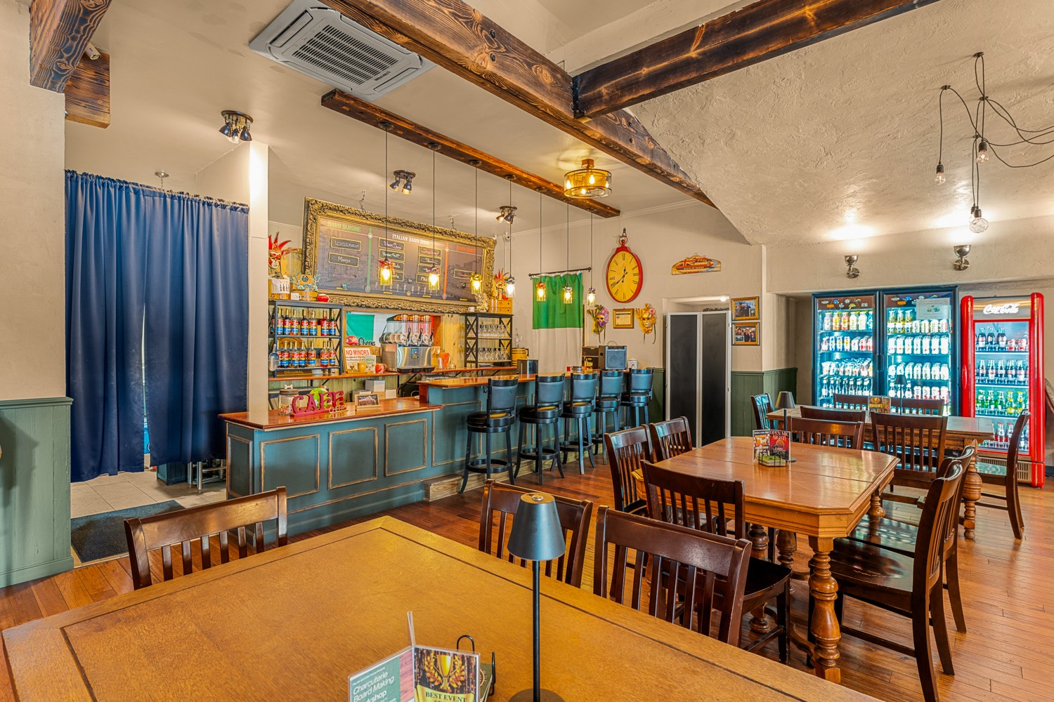 Bar area with blue counter, bar stools, tables, chairs, and vending machines in background.