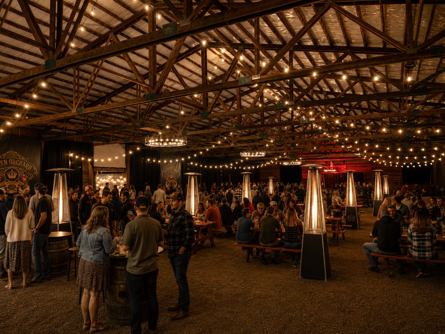 Indoor event with string lights, people standing and sitting at tables, warm lighting, and a high ceiling with exposed beams.