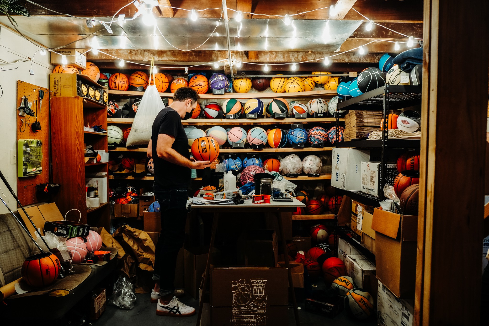 Person shopping for basketballs in a sports store with shelves full of various sports balls, shelves, and equipment.