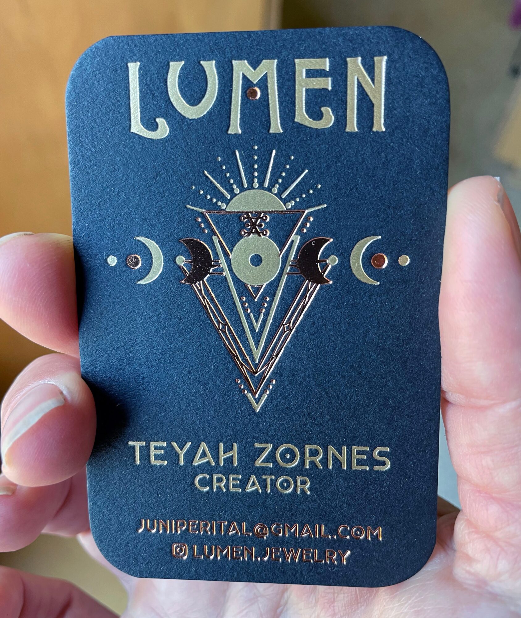 Blue card with white text and geometric design, held by a person's hand, with a blurred background.