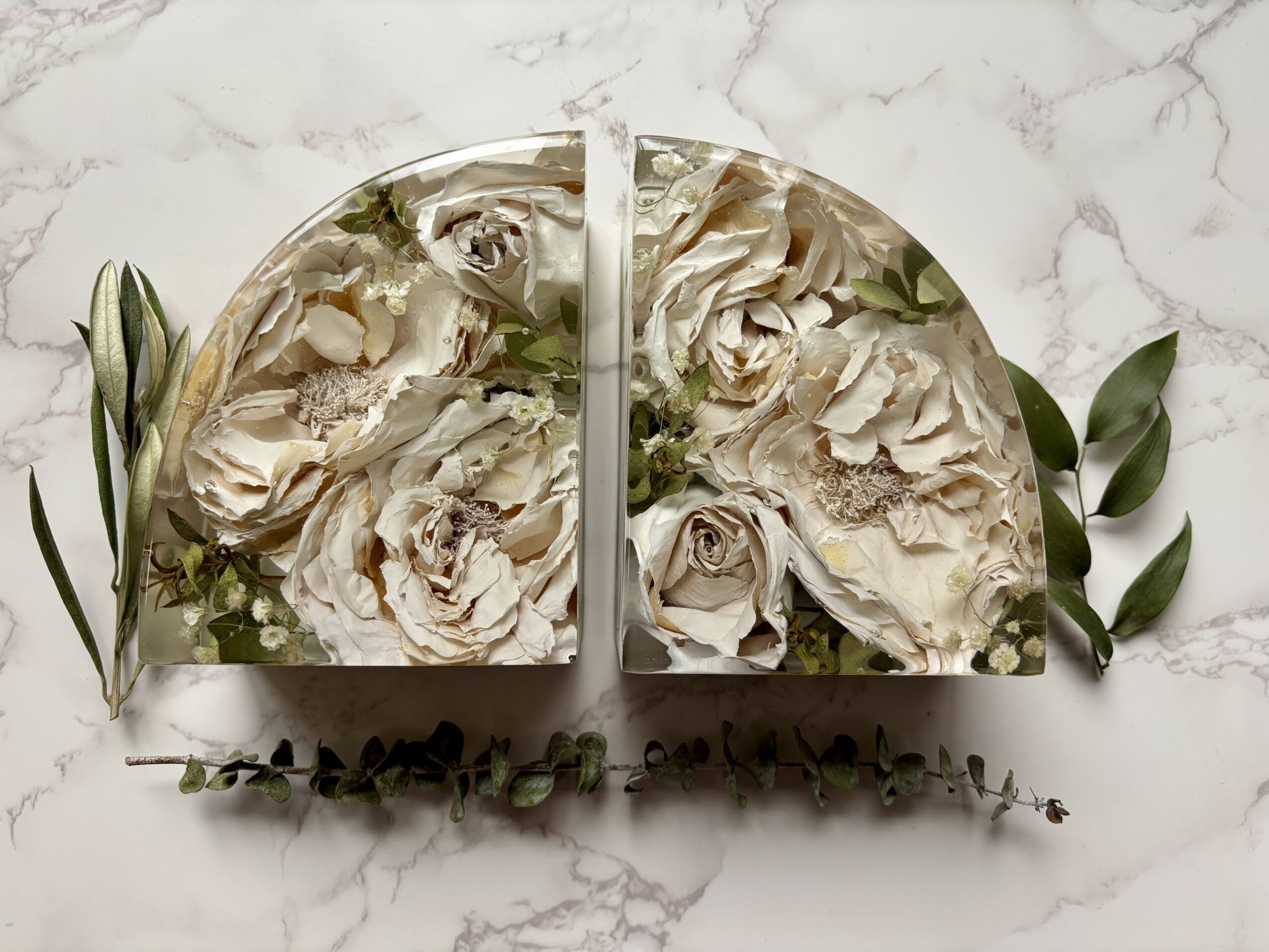 Two semi-circular floral arrangements with white roses and greenery on a marble surface.
