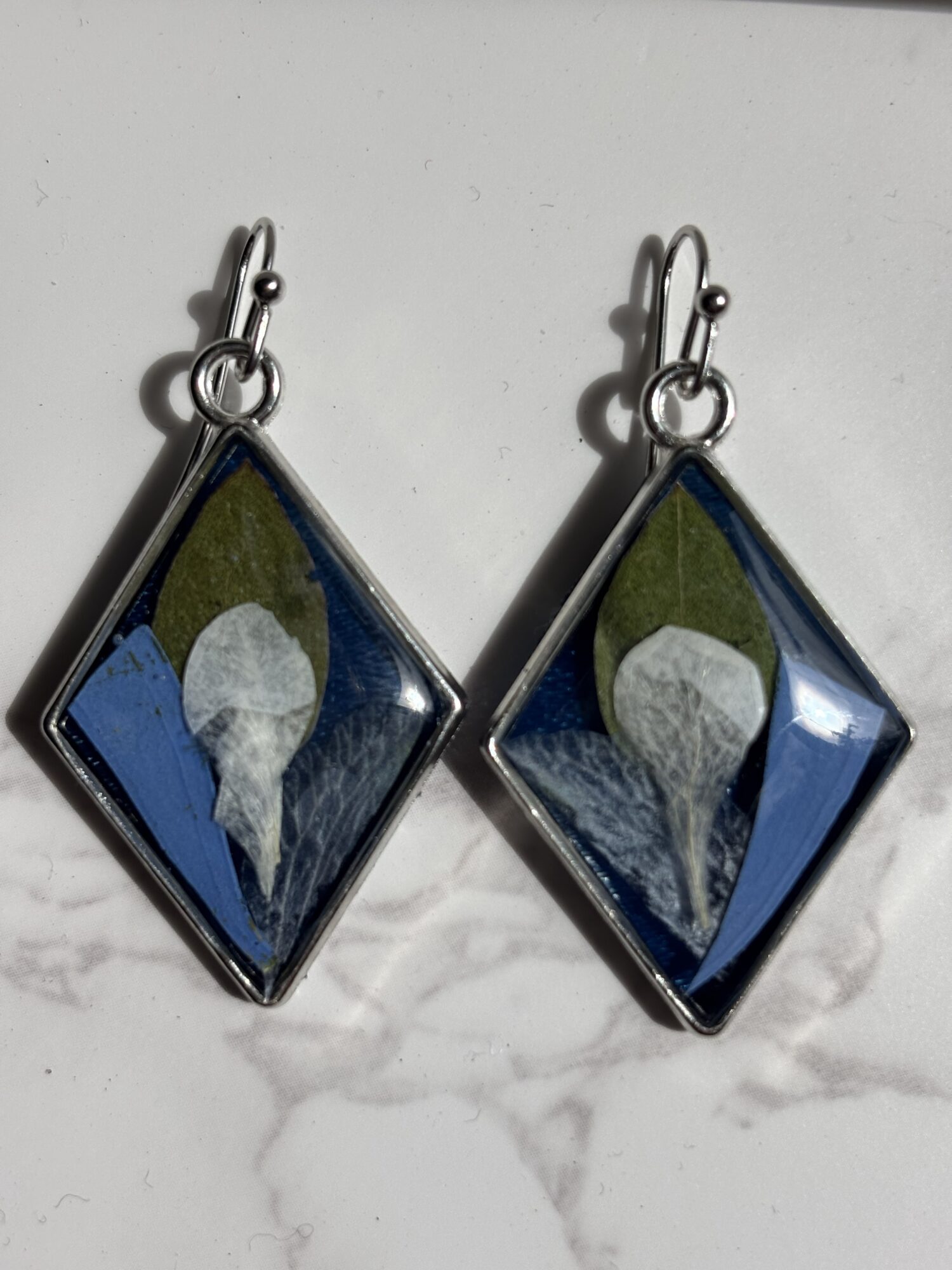 Pair of diamond-shaped earrings with blue, green, and white design, hanging against a white background.