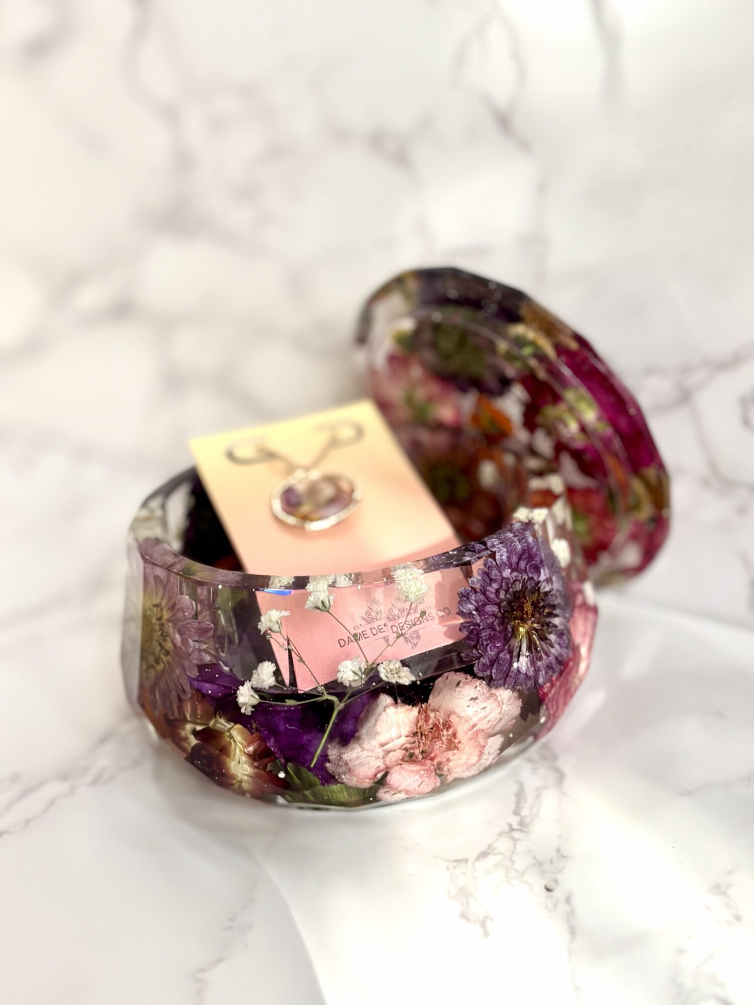 Open glass container with dried flowers inside, placed on a white marble surface.