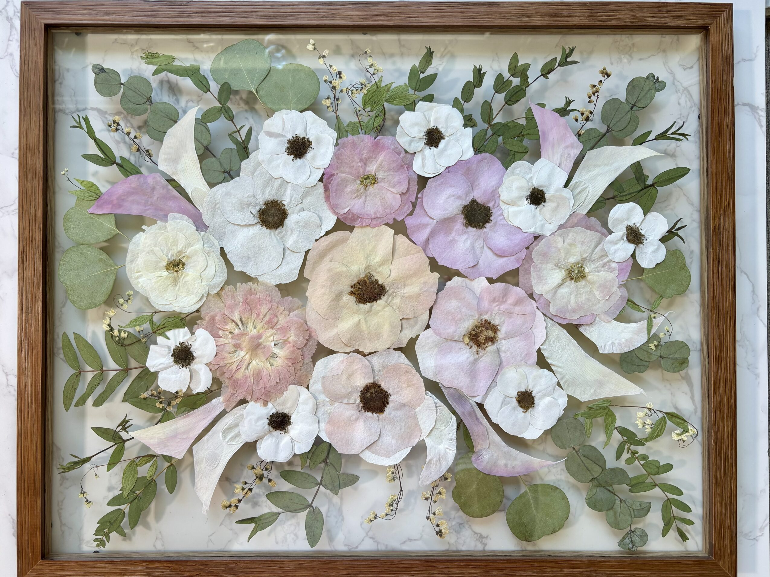 Framed floral artwork with white, pink, and purple flowers and green leaves, arranged symmetrically.