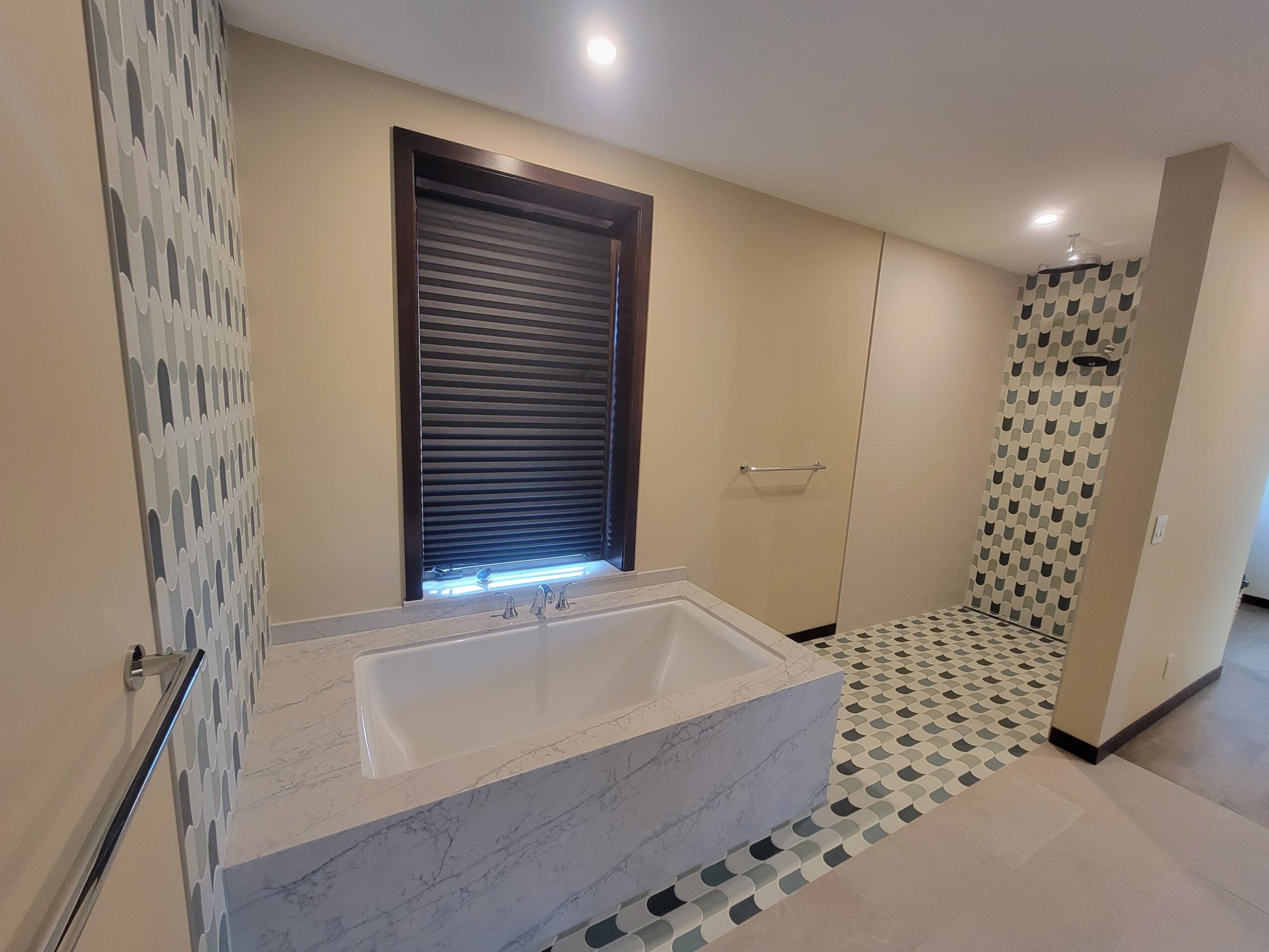 Bathroom with bathtub, window with blinds, and patterned tile floor and wall, ceiling light, and towel bar.