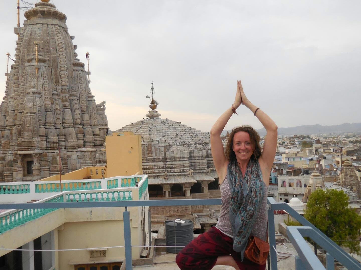 Woman standing on a rooftop with hands together above her head, cityscape and historic temple in background.