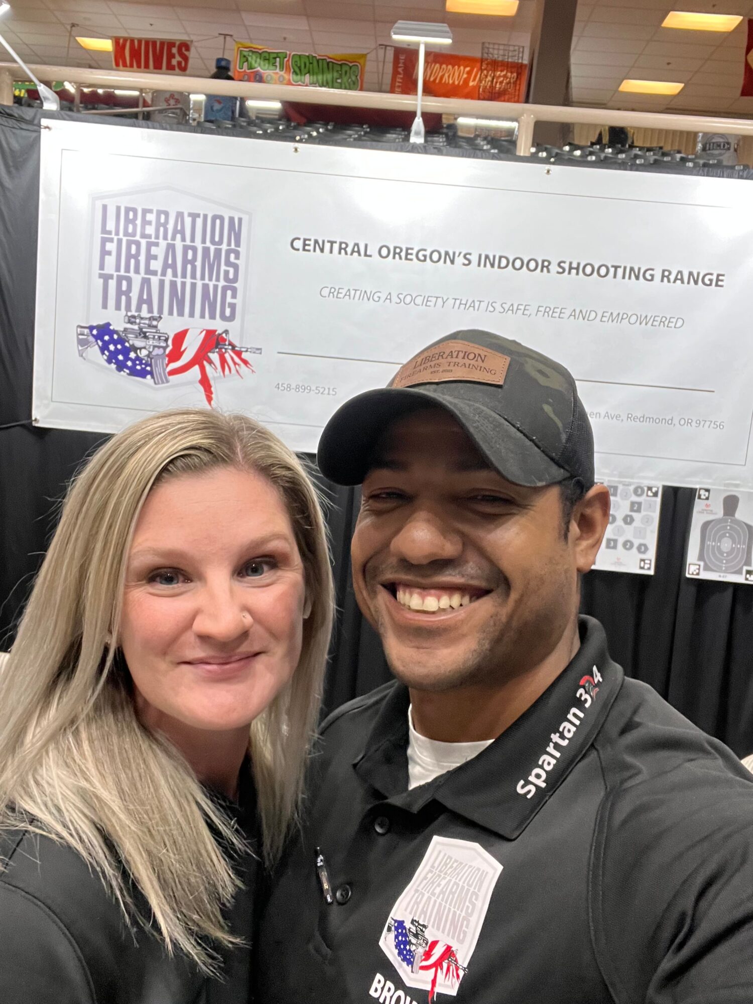 Two people smiling in front of a sign that reads 'Liberation Training' at a shooting range.
