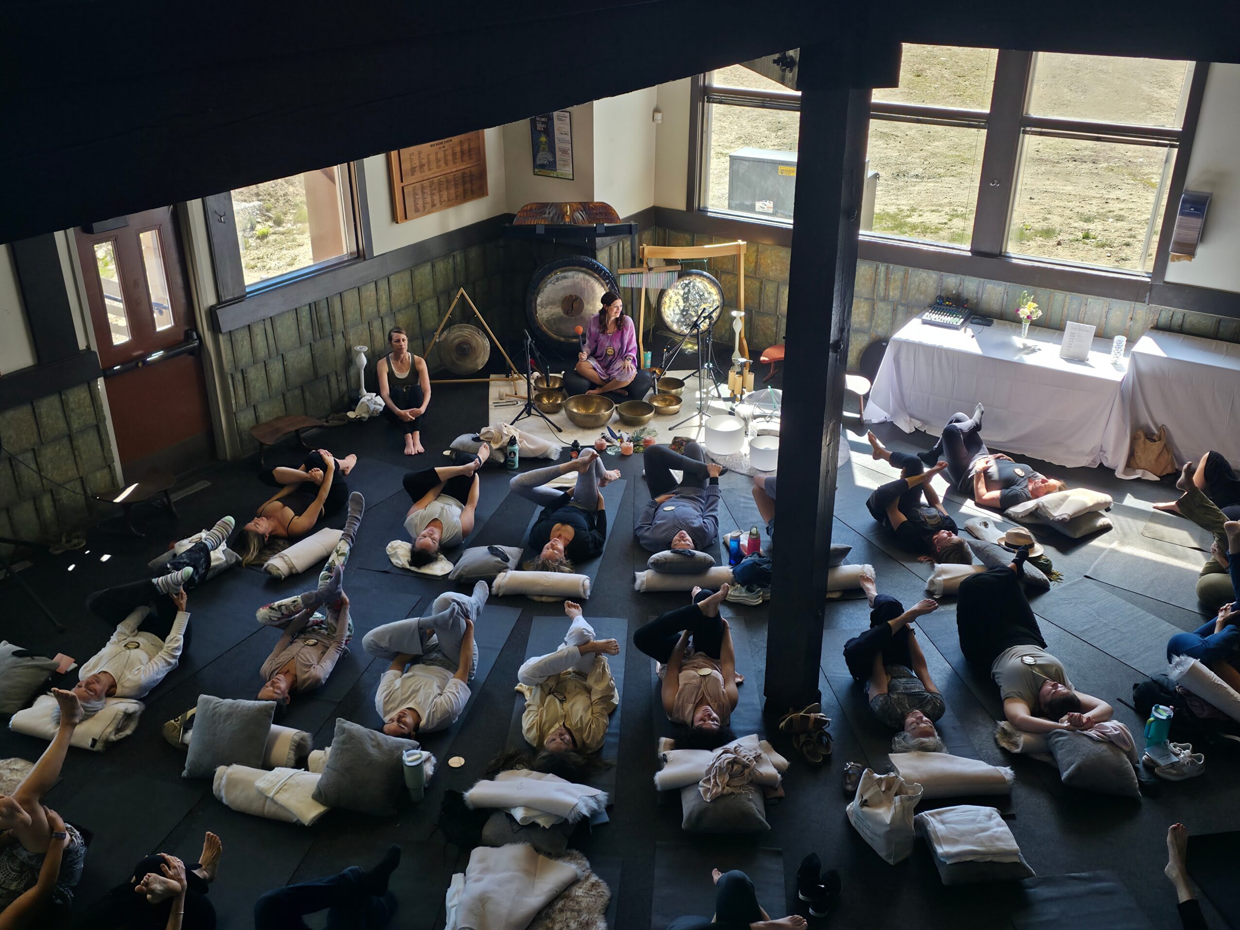 People lying on mats on the floor in a spacious room with large windows and natural light.