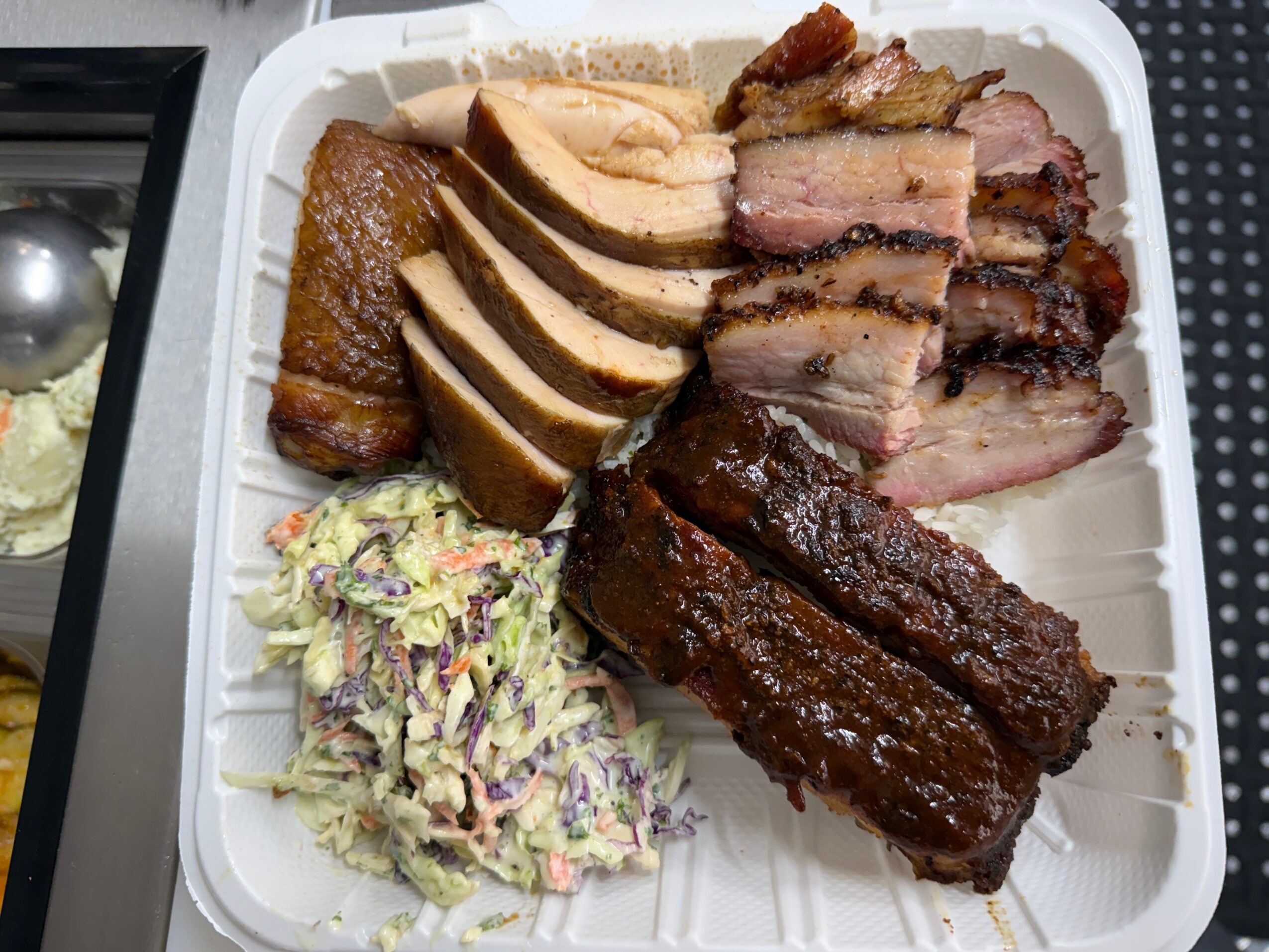 Assorted sliced meats, coleslaw, and glazed ribs on a white tray.