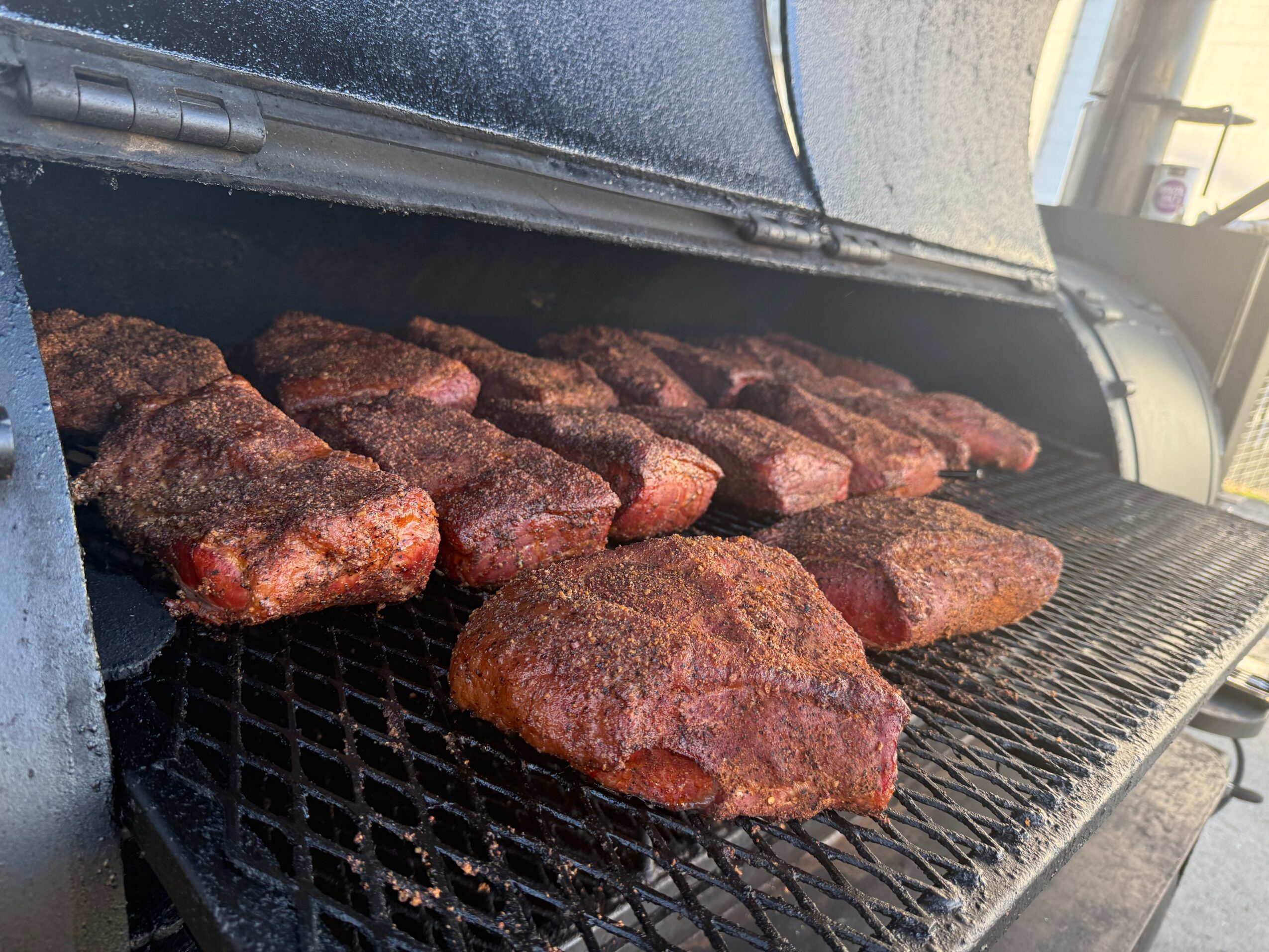Several pieces of meat are cooking on a grill, with some pieces appearing seasoned or marinated.