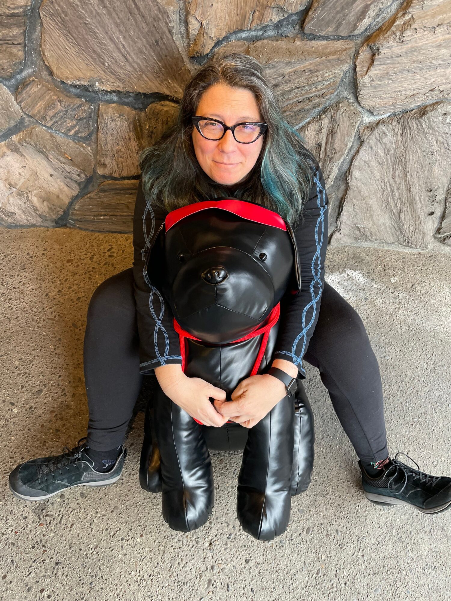 Person lying on ground holding a black helmet with red straps, next to a black bag, on a concrete surface.