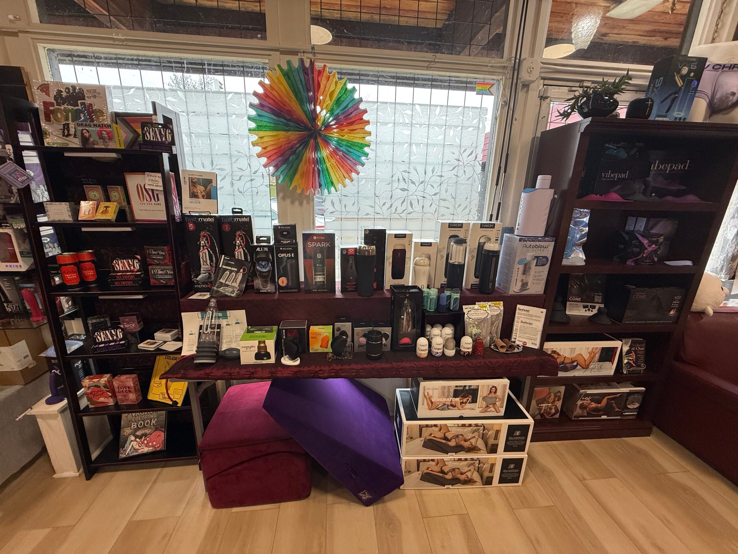 Bookshelves with various items, colorful wheel decoration, and a purple cushion in a store or library setting.