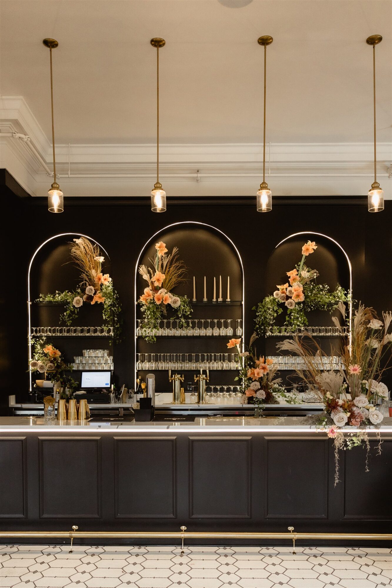 Elegant black display with floral arrangements and candles, illuminated by hanging pendant lights, on a patterned floor.
