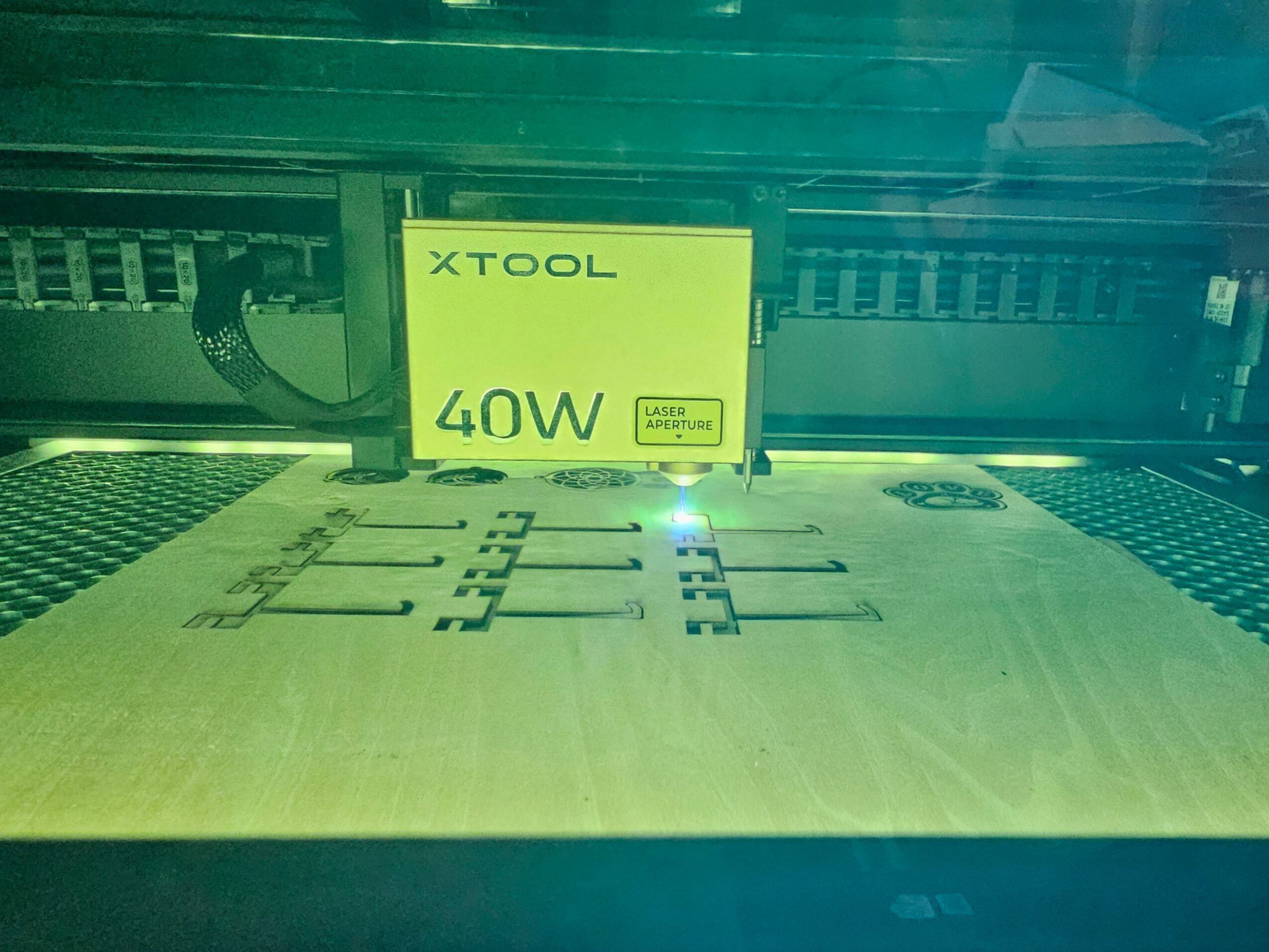 Laser cutting machine with a yellow sign reading 'XTOOL 40W' and a partially cut design on a sheet of material.