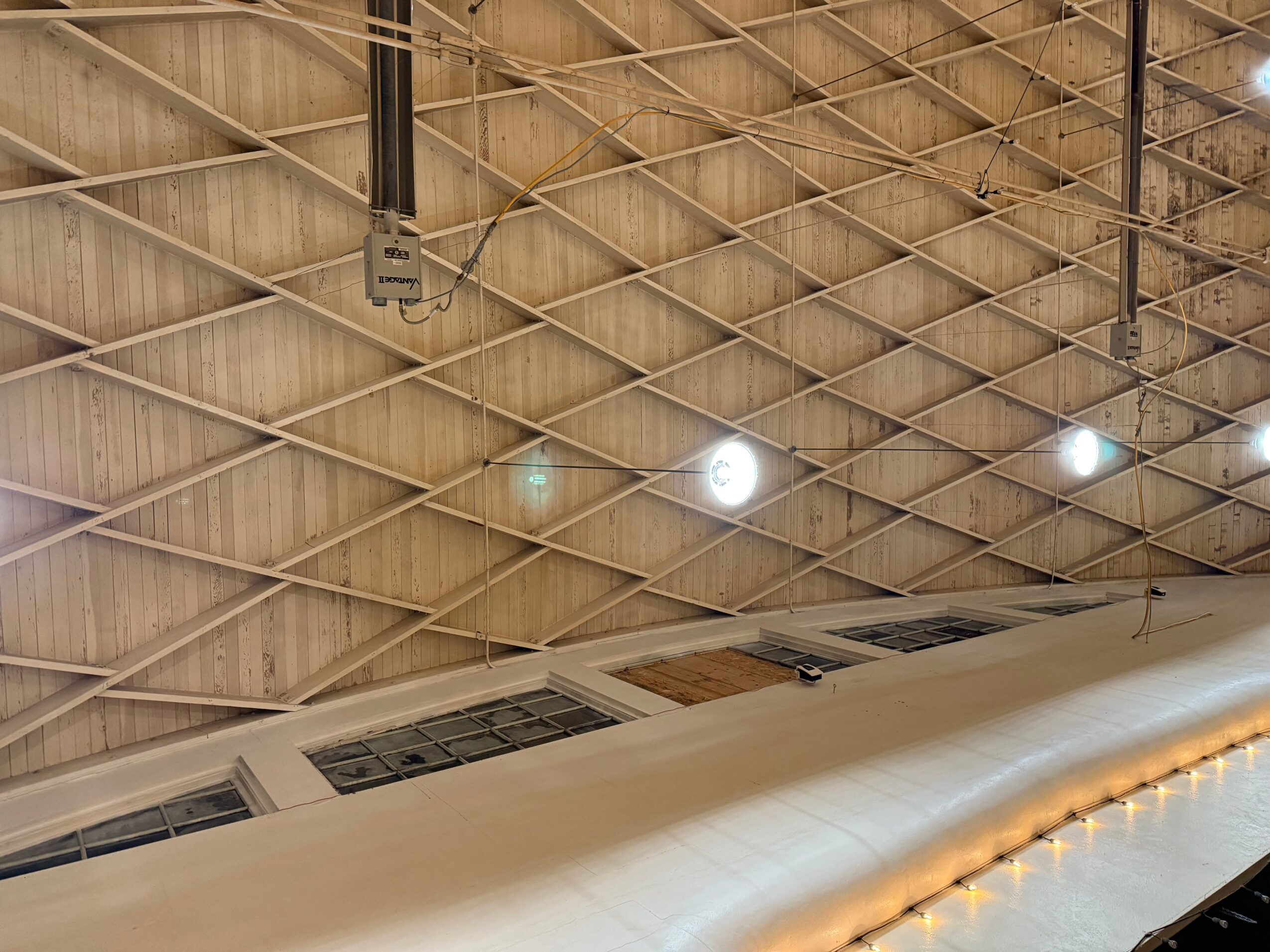 Ceiling with a diamond pattern, lights, and structural elements, with part of a large white object at the bottom.