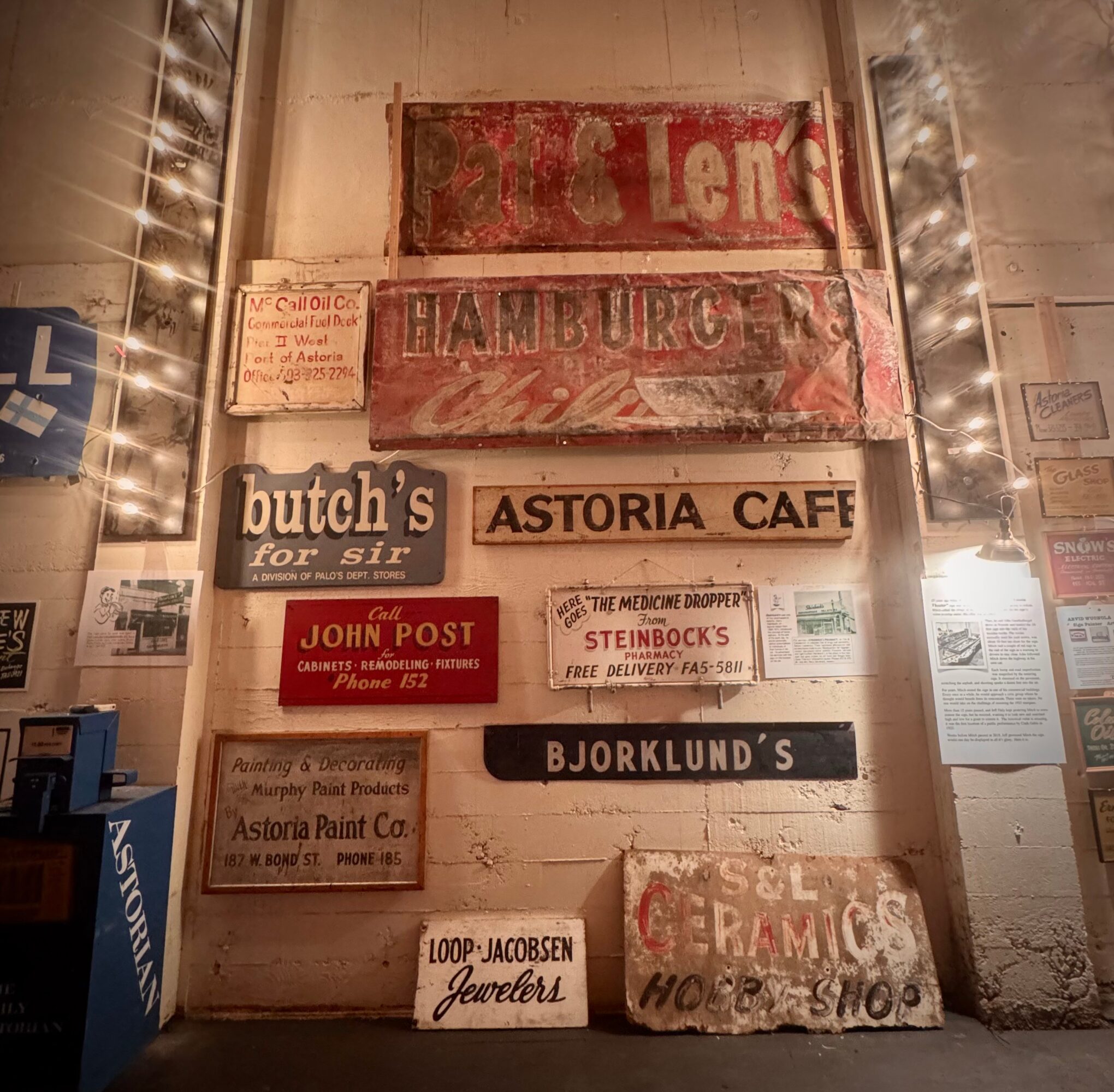 Wall with vintage signs and advertisements, including 'Astoria Cafe' and 'Bjorklund's', in a dimly lit space.
