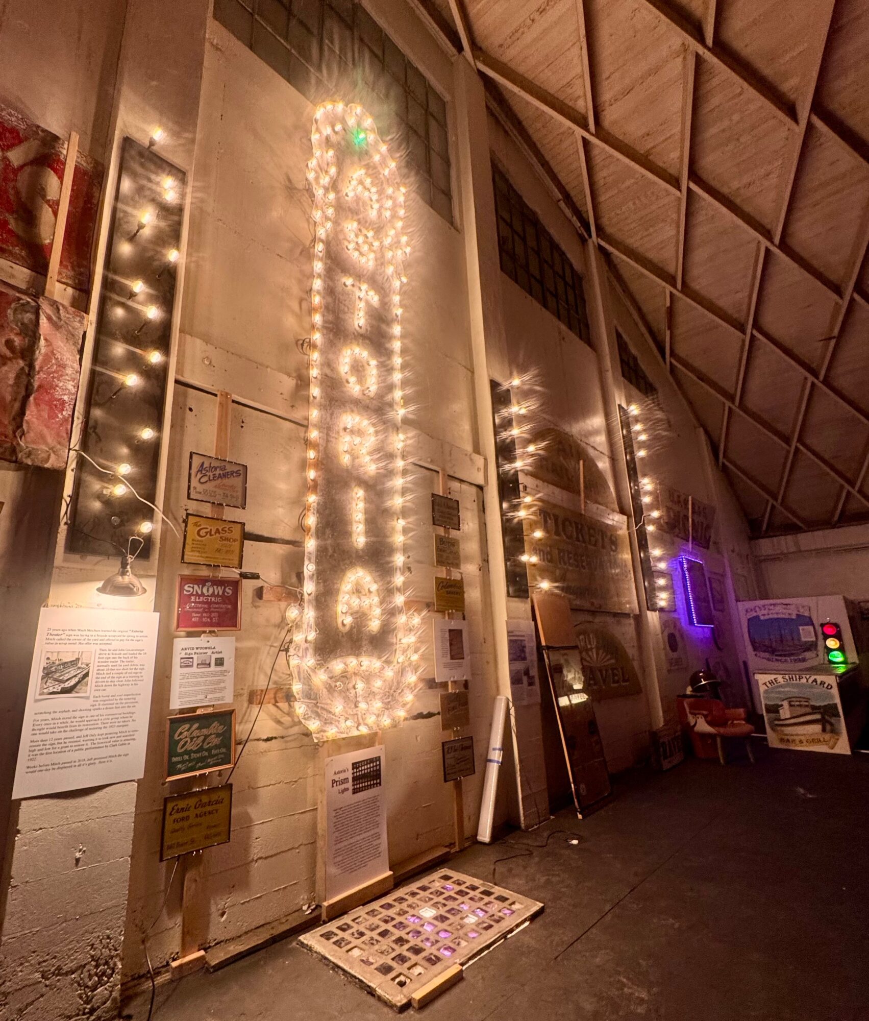 Interior of a building with a tall wall decorated with string lights and signs, and a sloped ceiling. Word 'BOUTIQUE' is illuminated with lights.