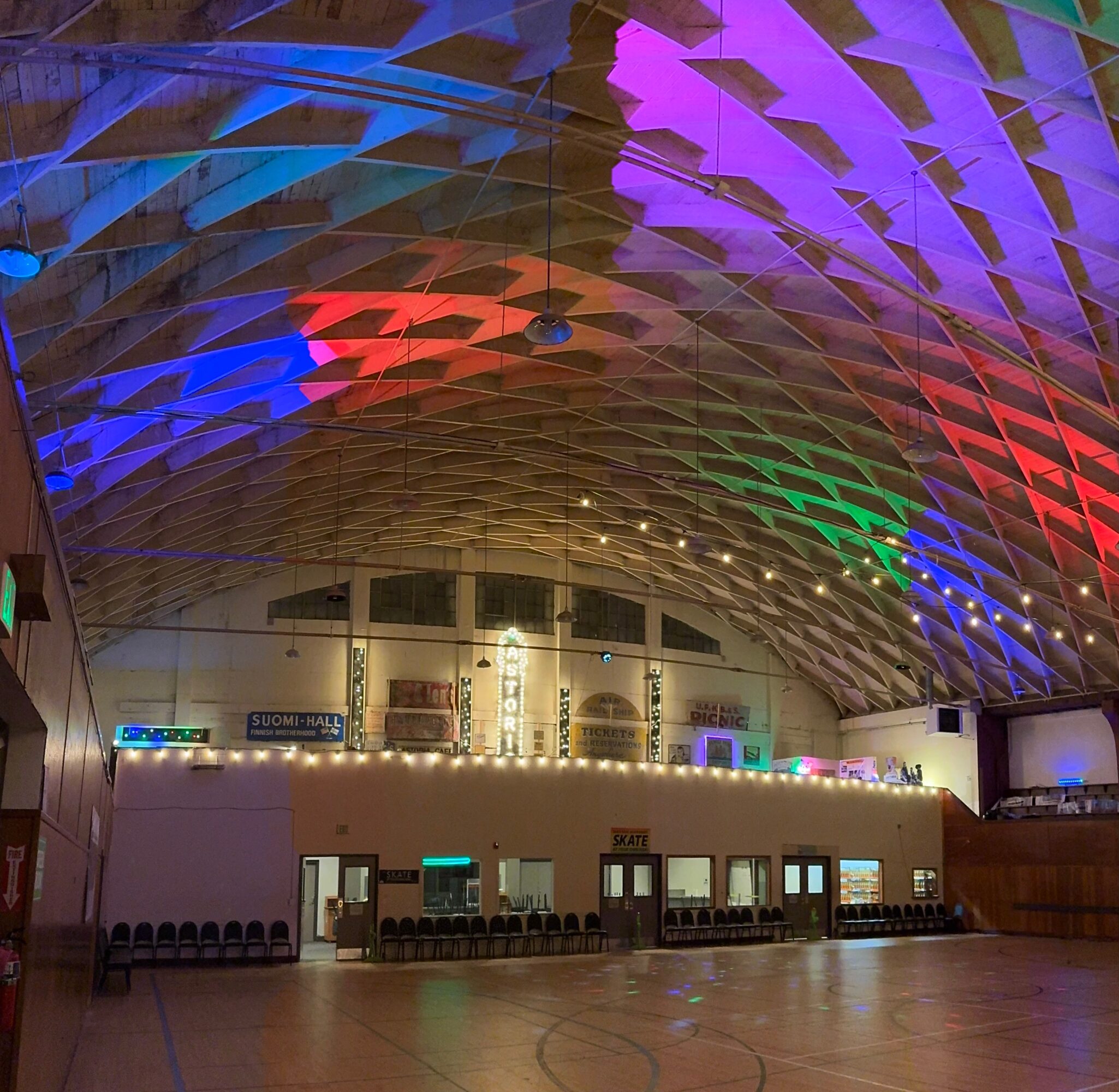 Indoor sports hall with a colorful, illuminated, arched ceiling and a row of chairs along the wall.