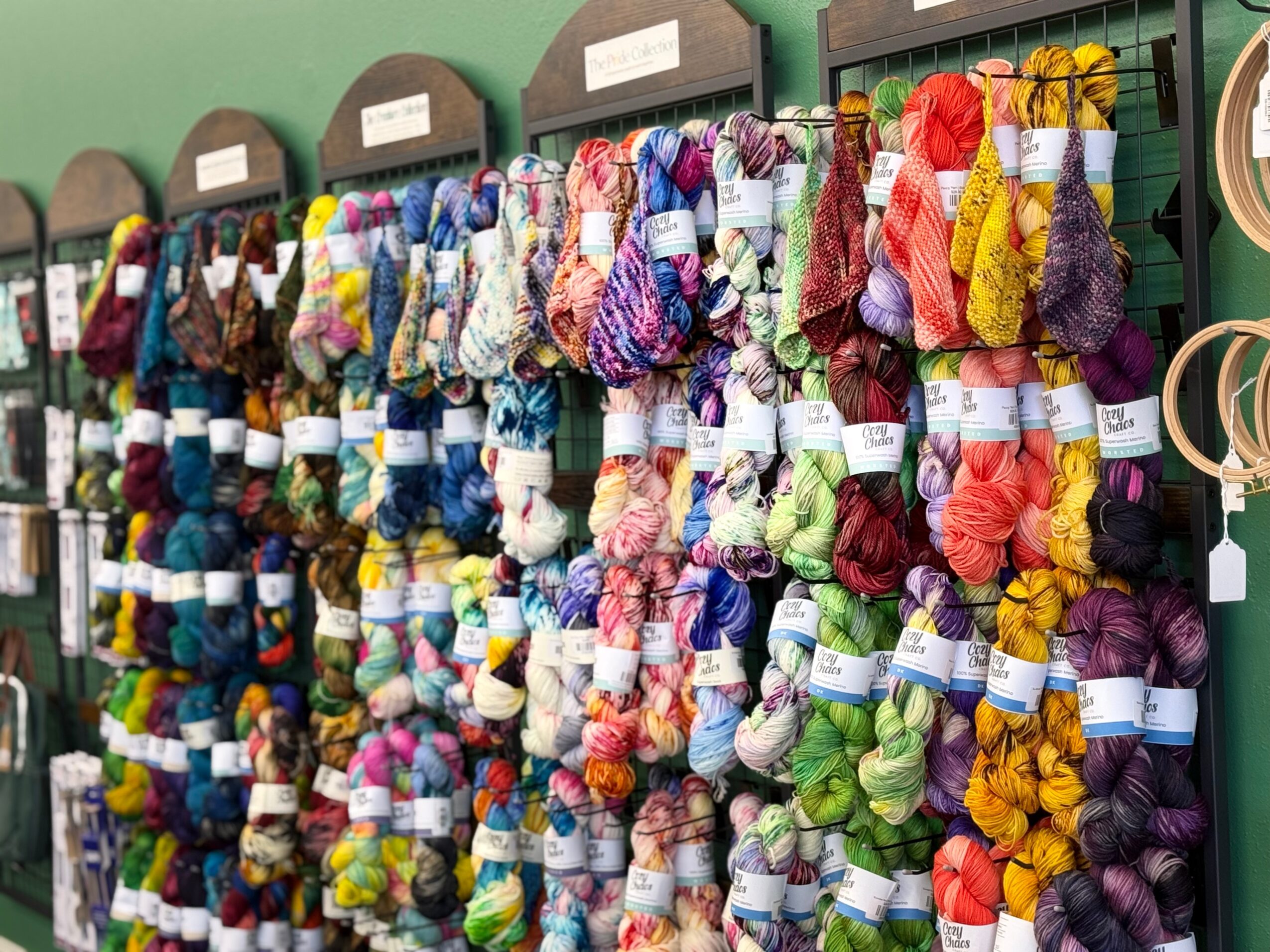 Display of colorful yarn skeins on shelves in a craft store, organized by color and type.