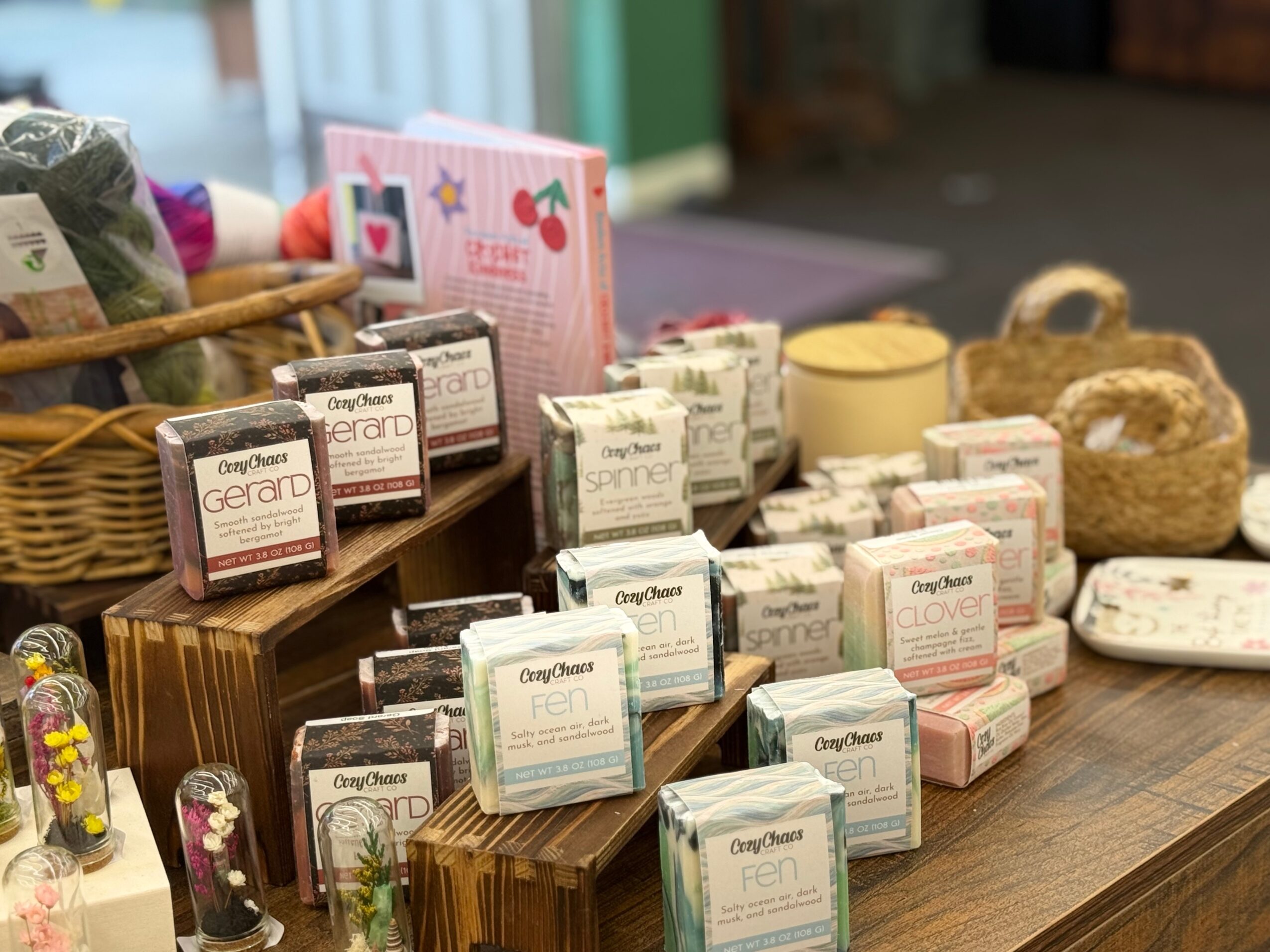 Various soap bars and skincare products arranged on a wooden table with baskets and packaging in the background.