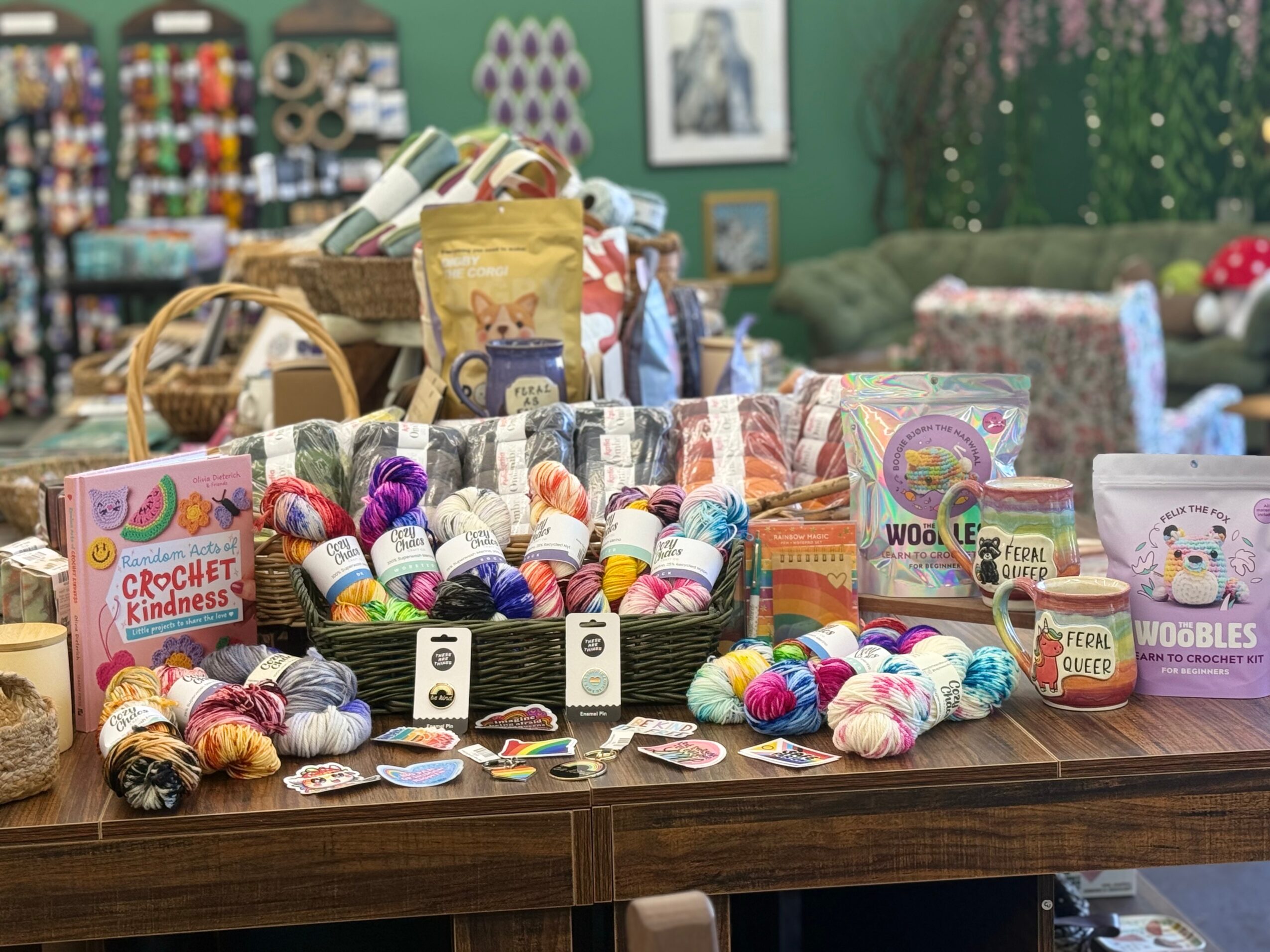 Display of colorful yarn balls, crochet kits, and craft supplies on a wooden table in a craft store.