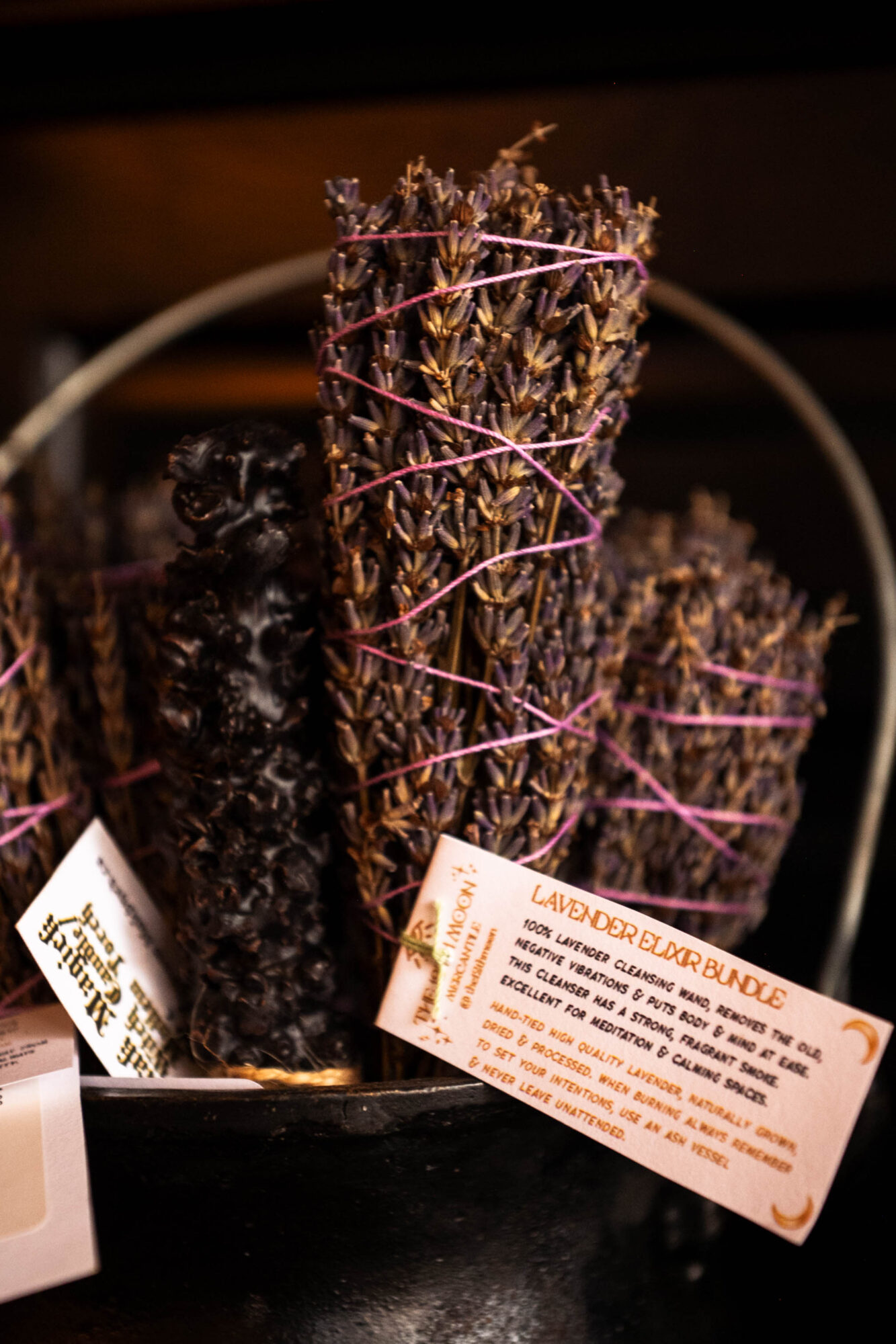 Bundles of dried lavender tied with pink string, with informational tags attached, in a container.