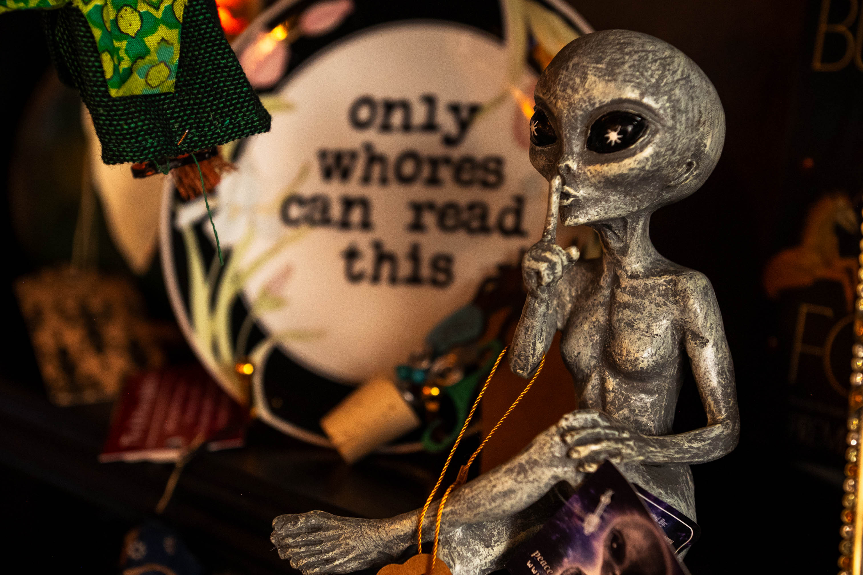 Alien figure with large eyes and metallic body holding a string, with a sign reading 'only whores can read this' in the background.