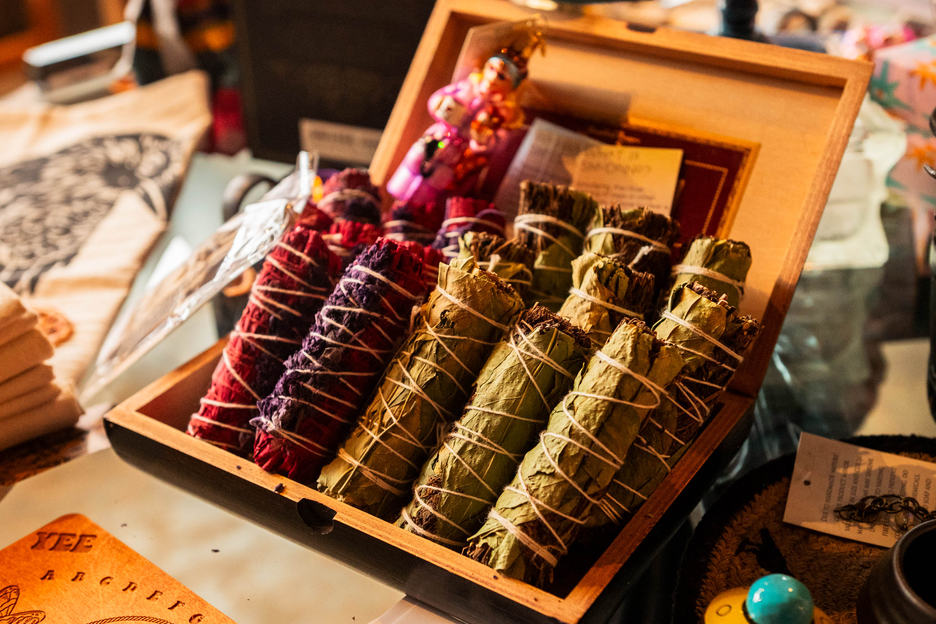 Open box with colorful wrapped bundles, possibly herbs or spices, on a table with various items around.