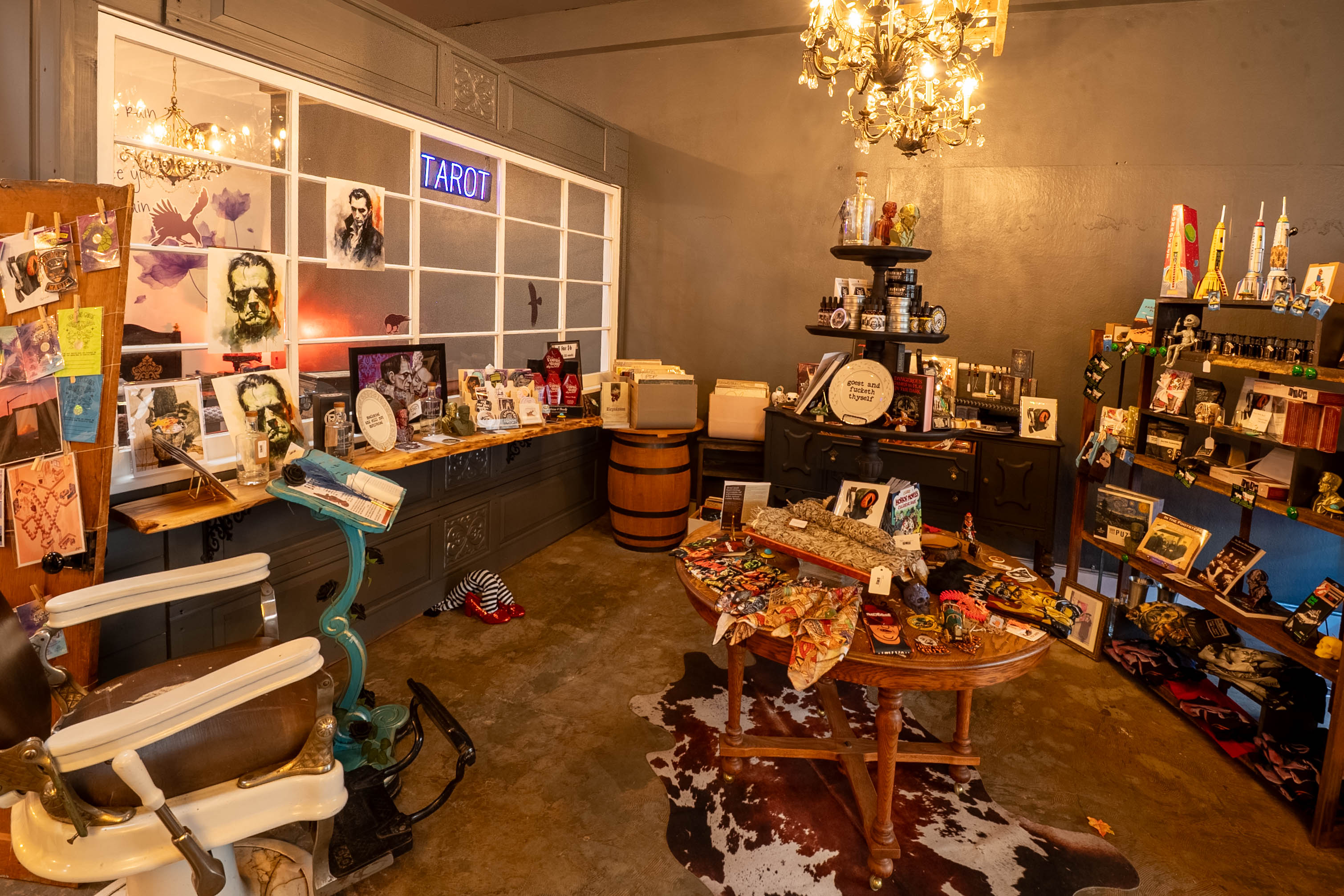Room with shelves of vinyl records, artwork, and decorative items, illuminated by a chandelier, with a table and various displays.