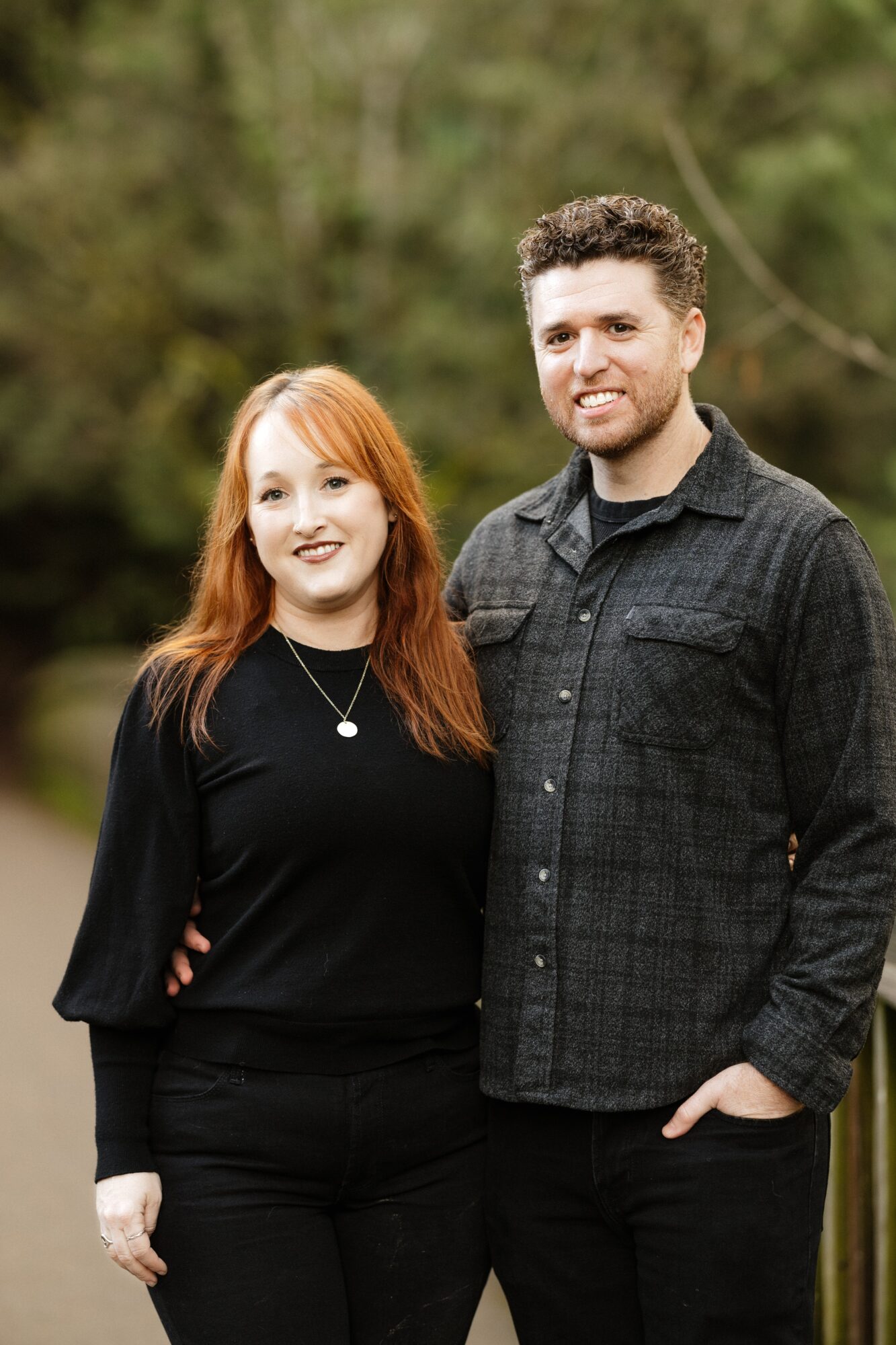 A smiling man and woman stand outdoors with trees in the background, posing for a photo.