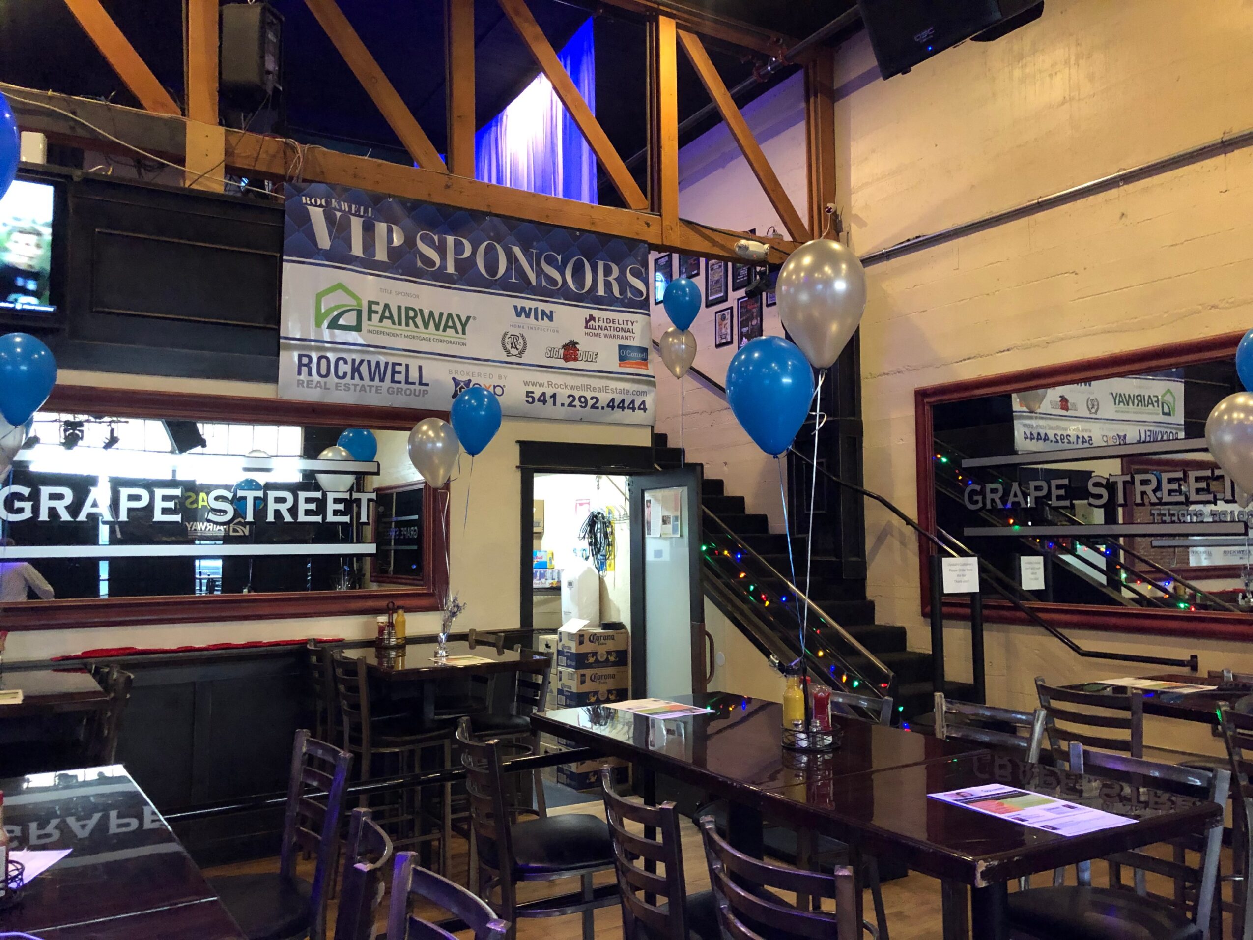 Indoor event space with tables, chairs, balloons, and a staircase, decorated for a celebration or gathering.
