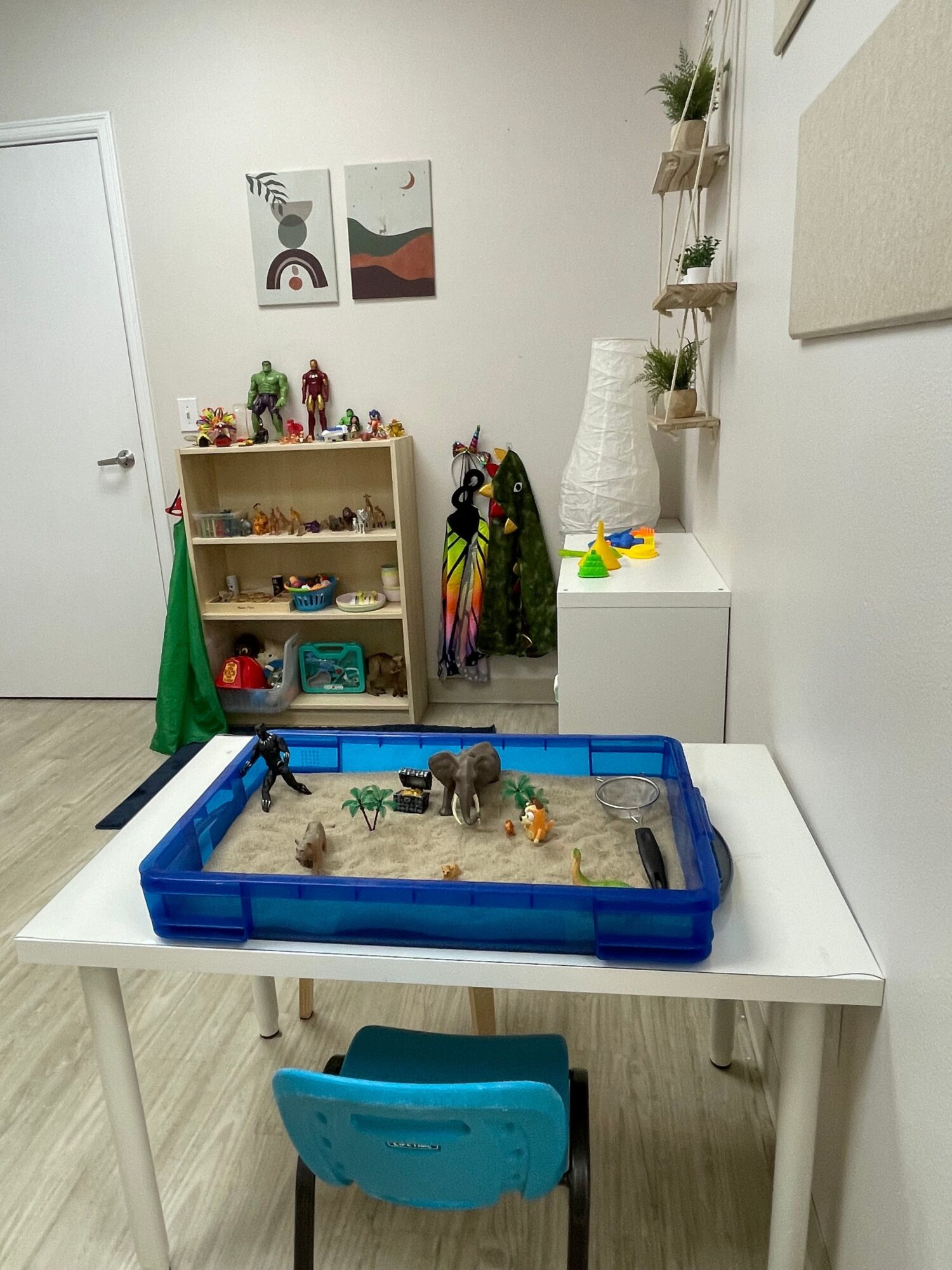 Children's play area with a sand table, blue chair, and shelves with toys and decorations in a room.