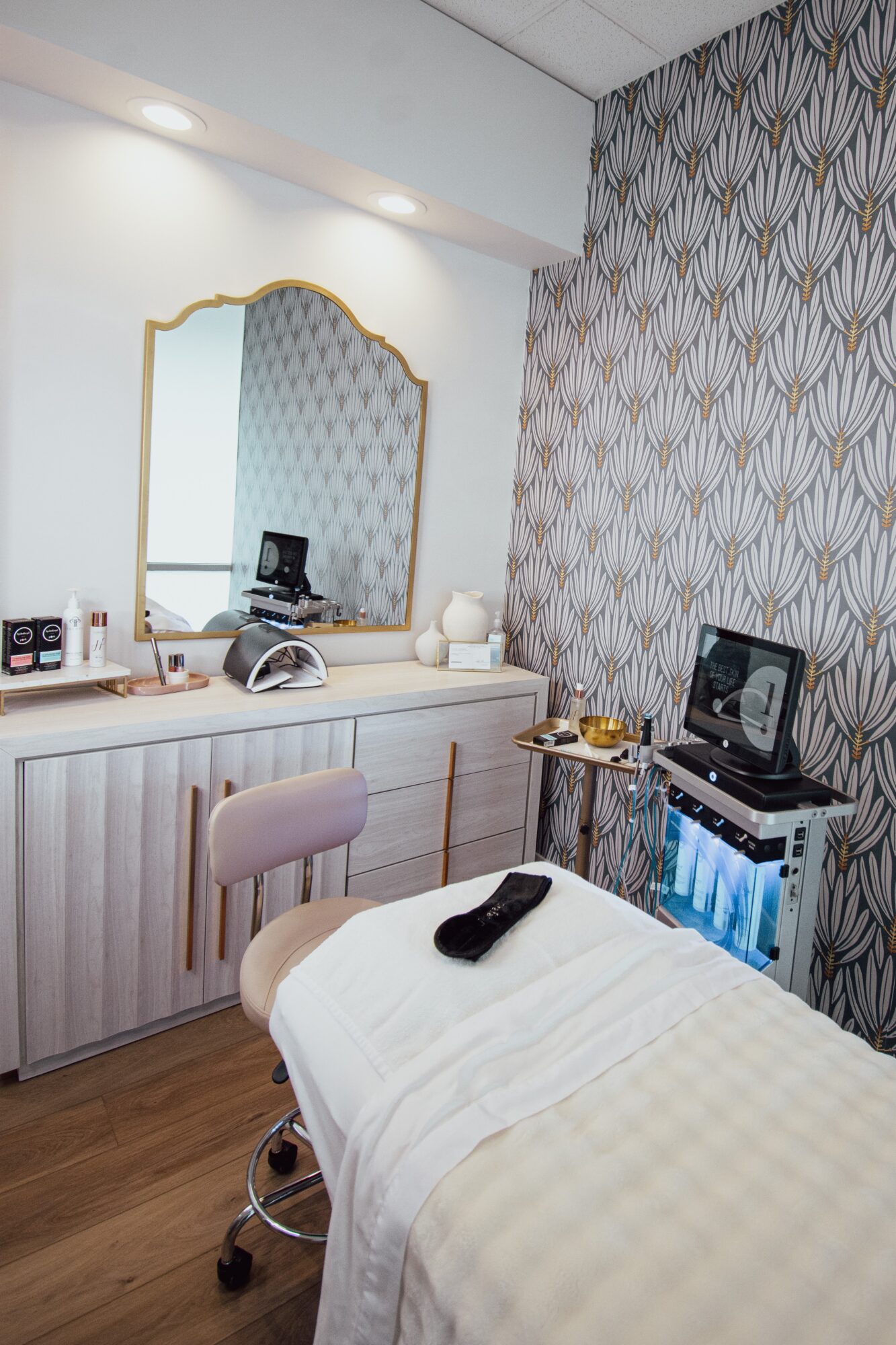 Hotel room with a bed, mirror, desk, and patterned wallpaper, featuring a small table with a TV and a remote control.