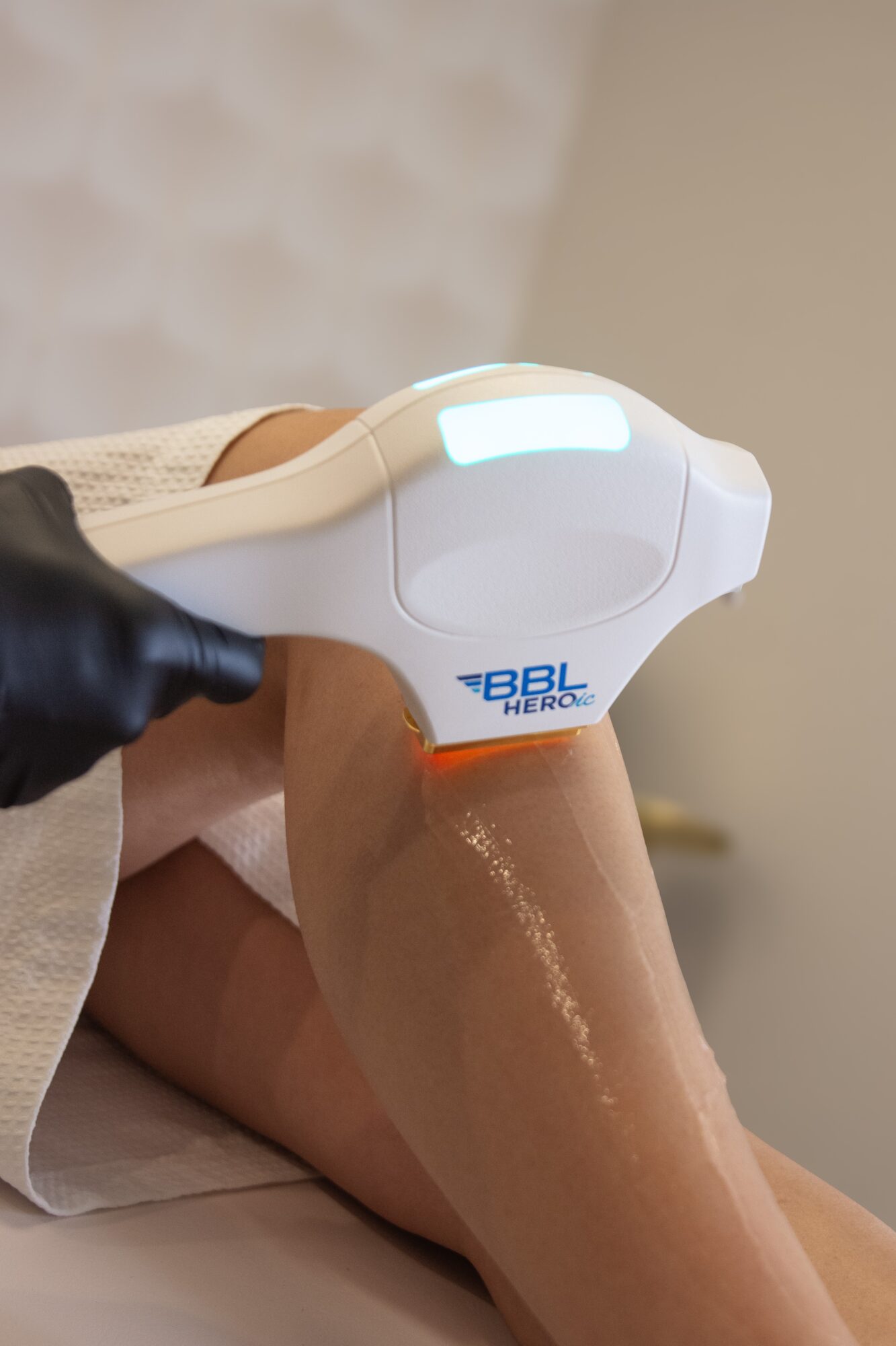 Medical device applied to a person's knee, with a healthcare worker wearing a glove holding it, in a clinical setting.