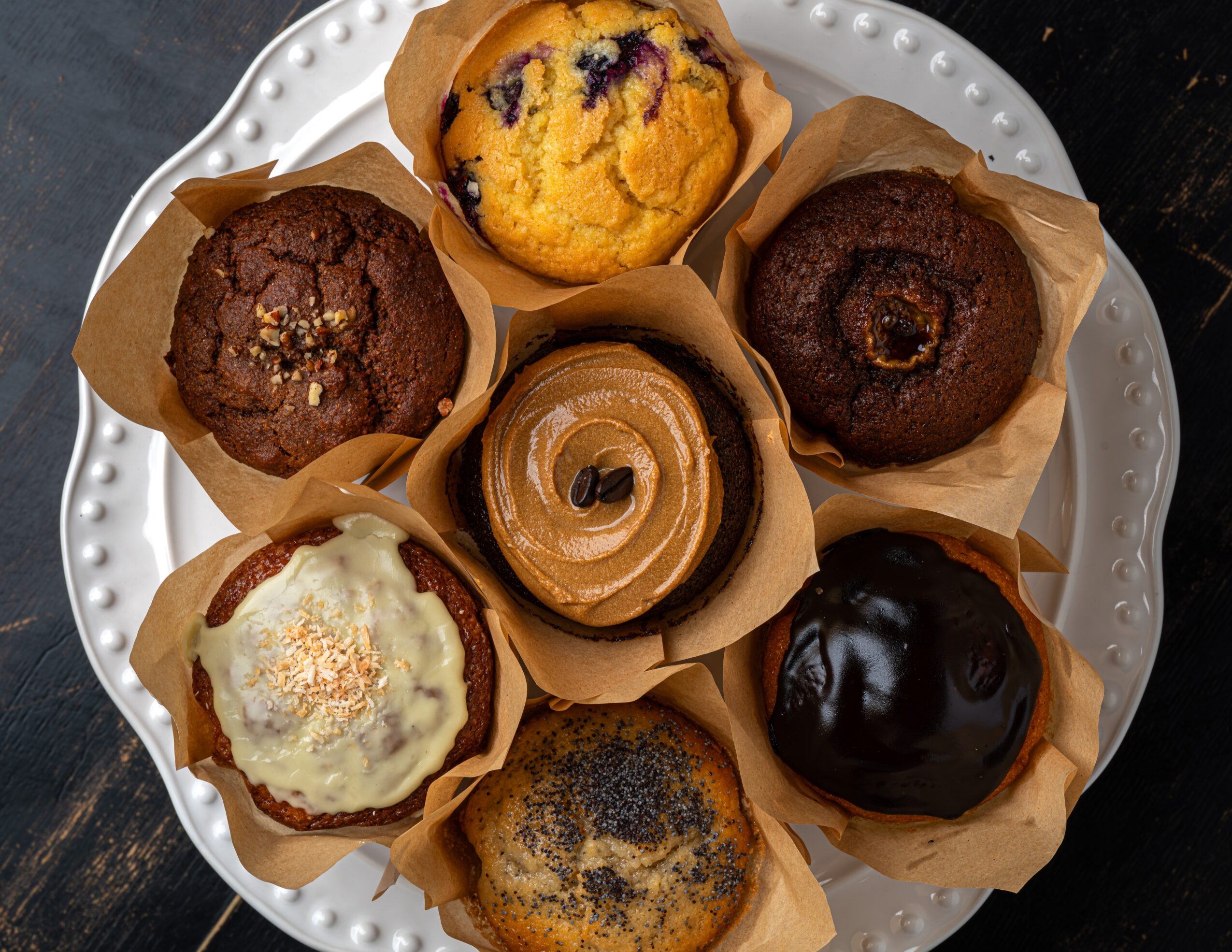 Plate with nine muffins and a cupcake, some with toppings, in paper liners, on a white dish.