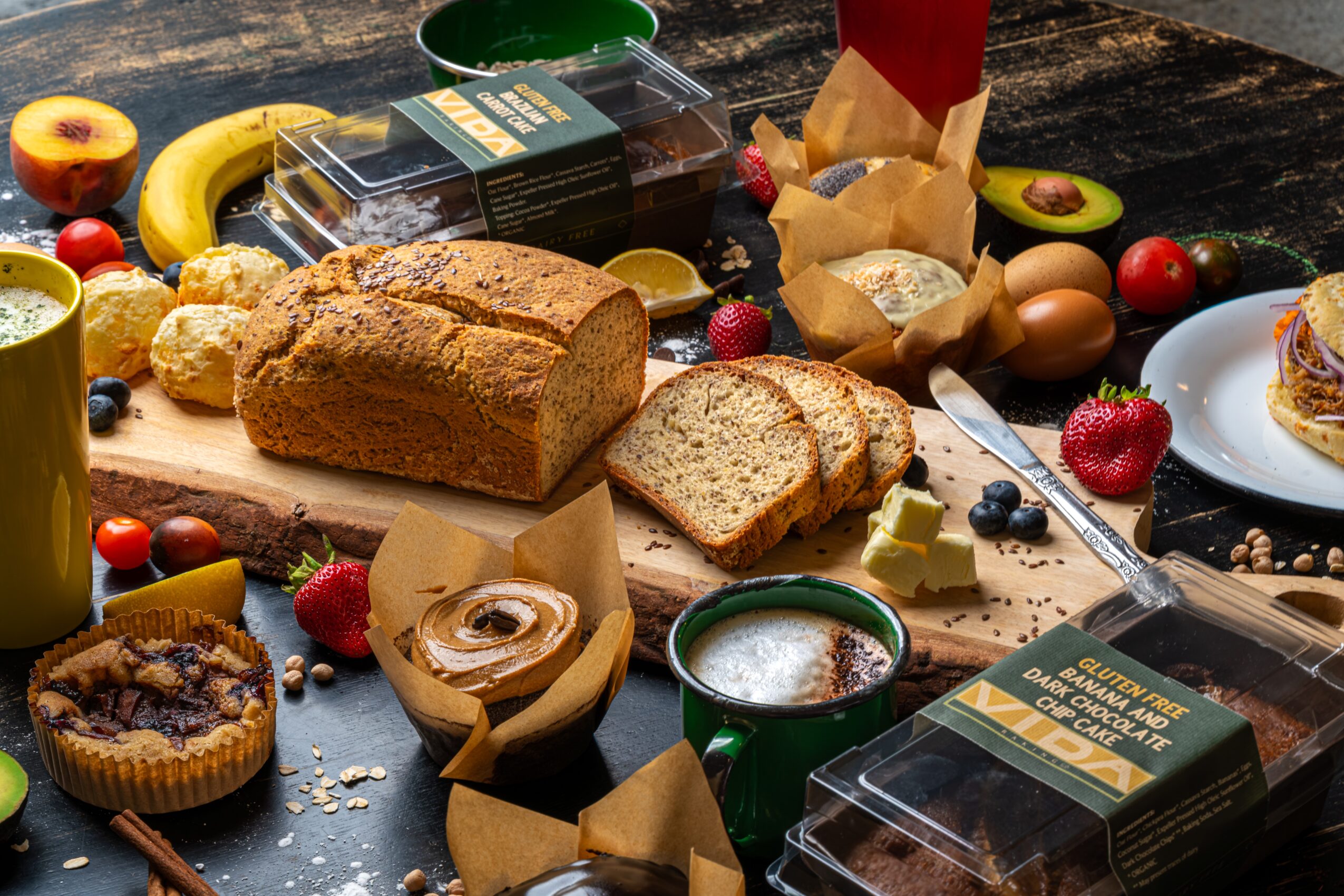 Breakfast spread with bread, muffins, fruits, eggs, and beverages on a wooden table.