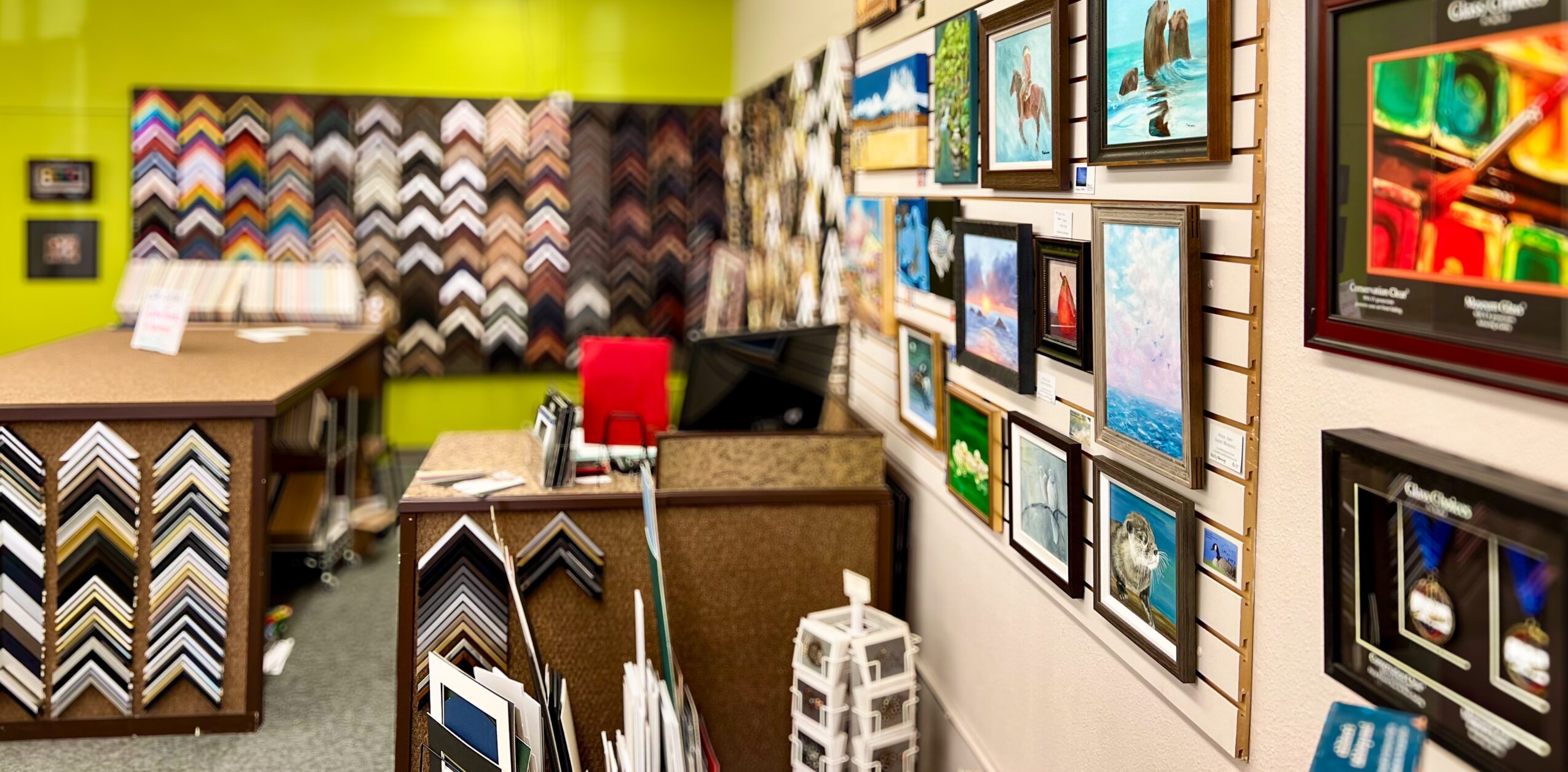 Display of various picture frames and samples in a store, with a table and chairs in the background.