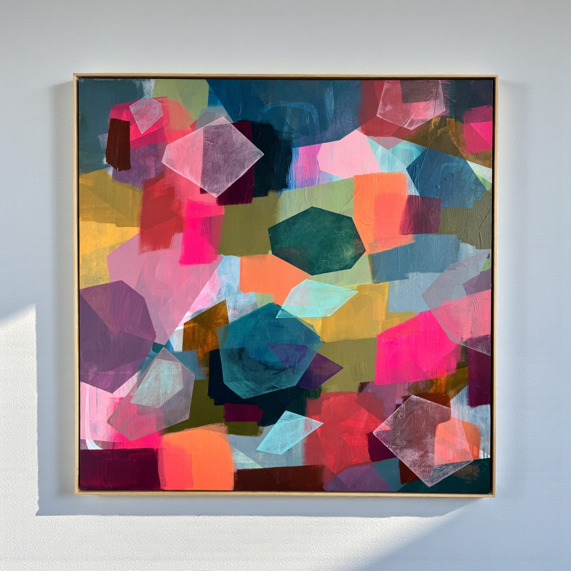 Abstract painting with colorful geometric shapes including pink, blue, green, and yellow on a white wall.