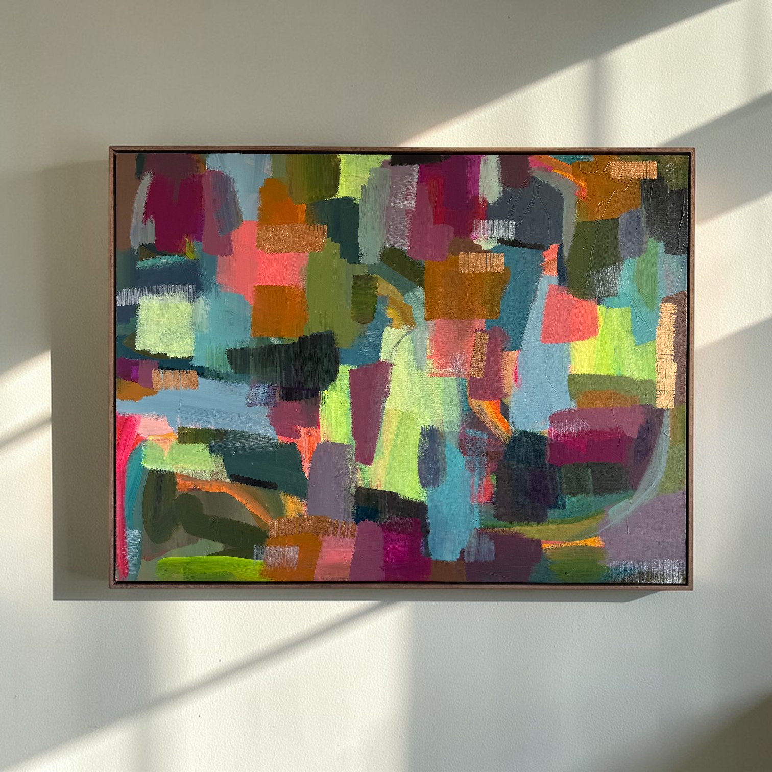Colorful abstract painting with various shapes and brushstrokes on a wall, illuminated by sunlight, with a shadow cast on the wall.