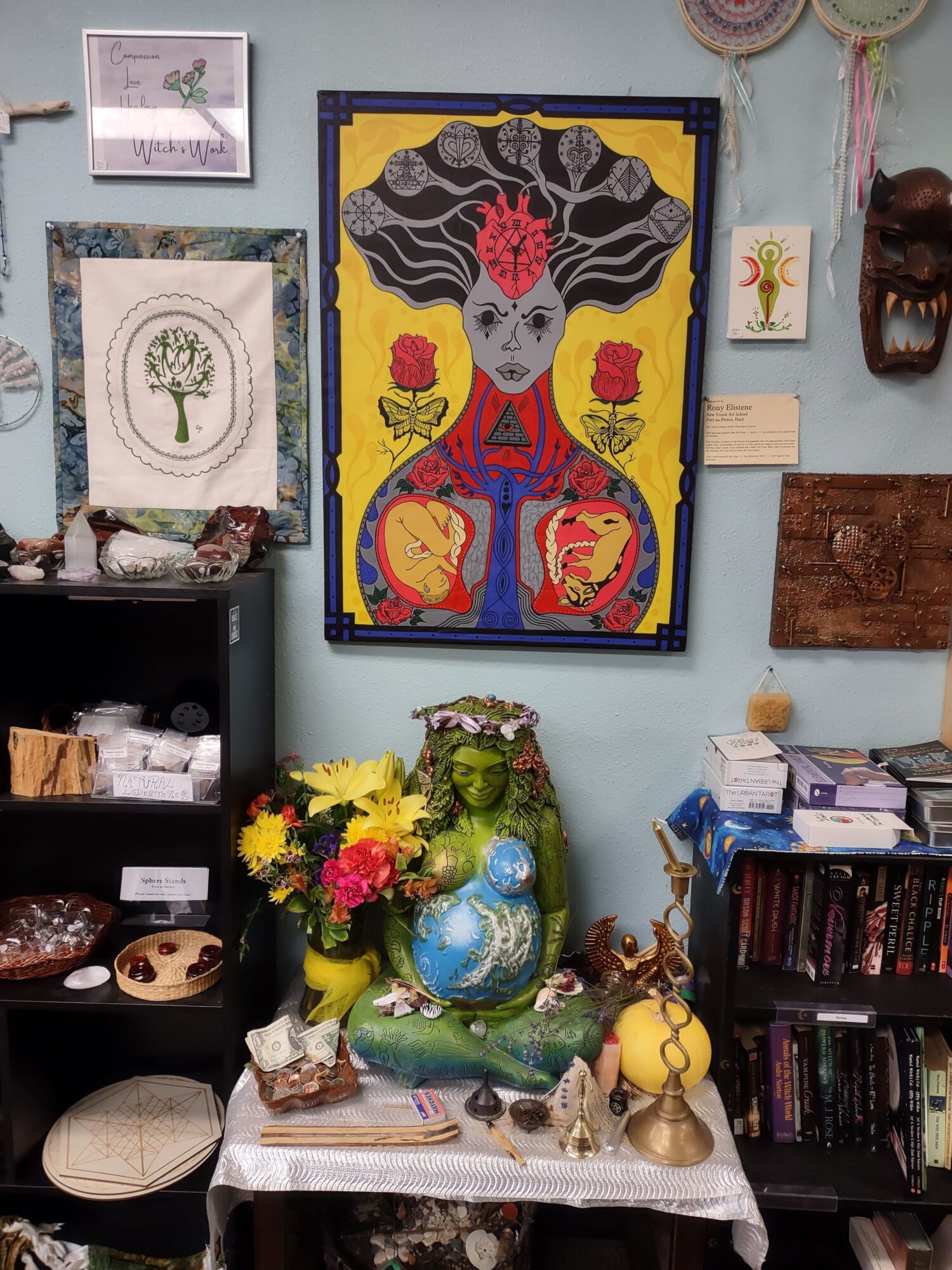 Decorative table with flowers, a globe, and various objects, with a colorful framed artwork on the wall behind.