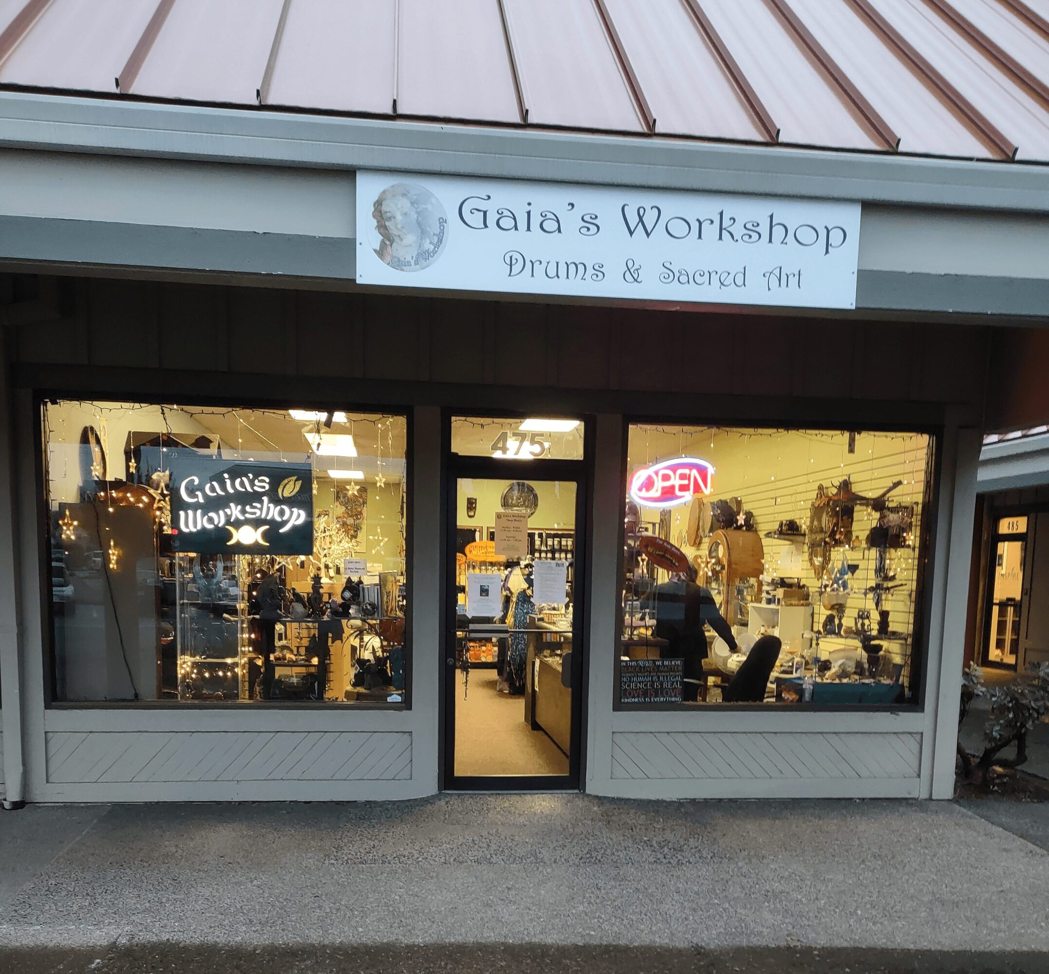 Storefront with sign reading 'Gaia's Workshop Drums & Sacred Art' and large windows showing inside displays.