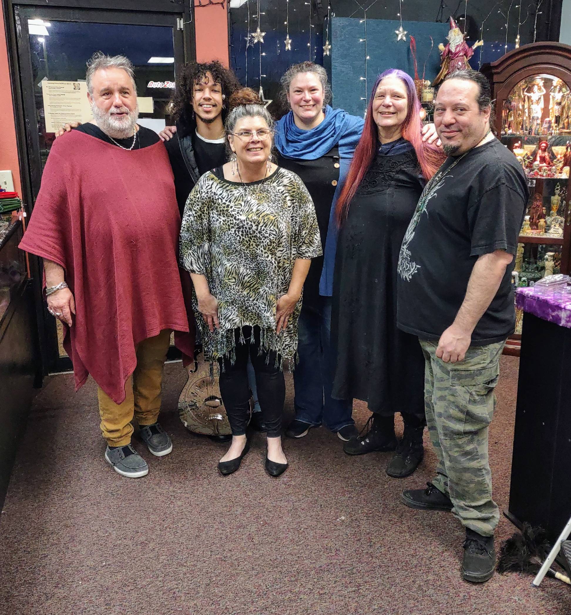 Group of six people standing indoors, smiling, with festive decorations in the background.