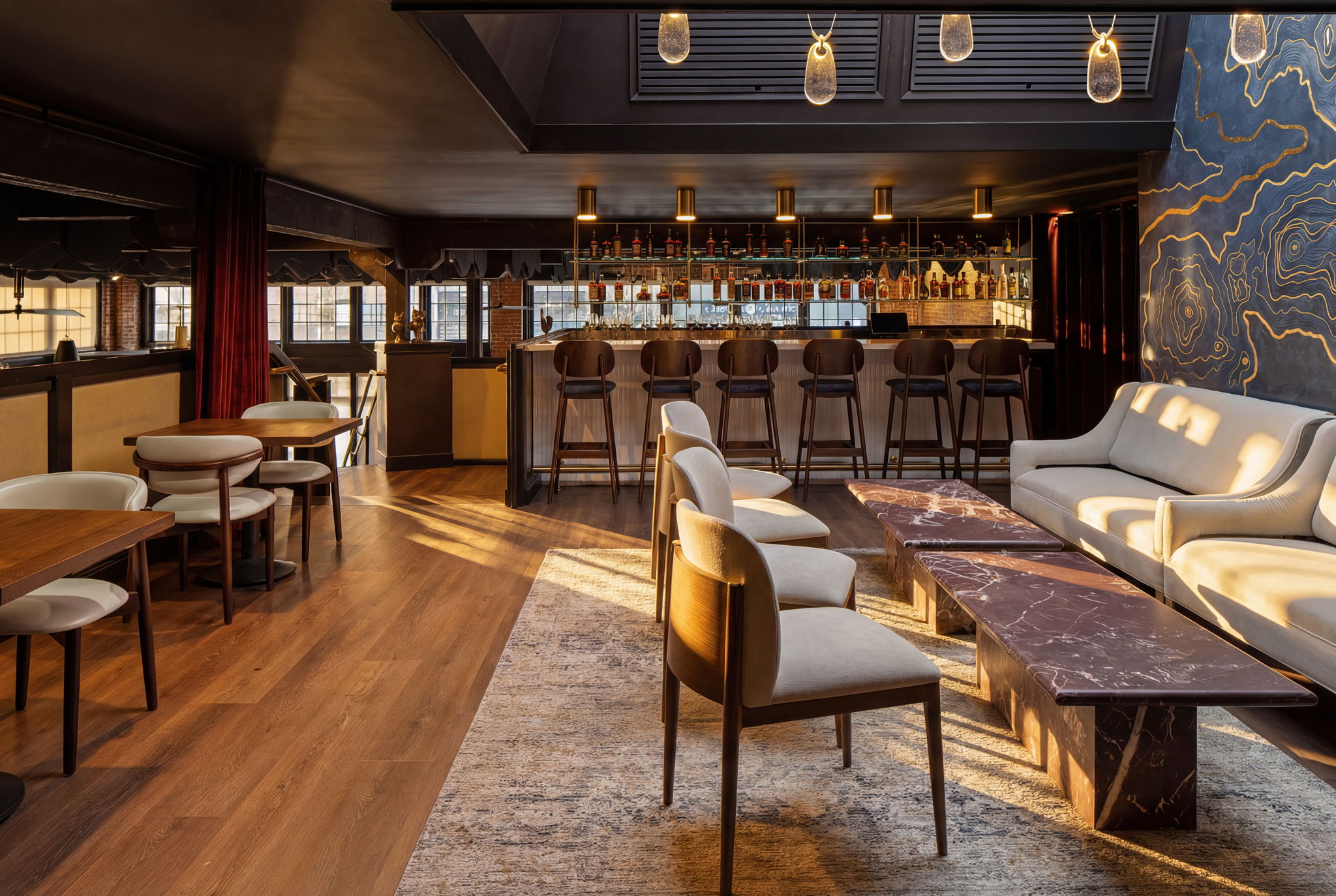 Elegant bar area with seating, a marble-topped table, and a white sofa, illuminated by warm lighting.